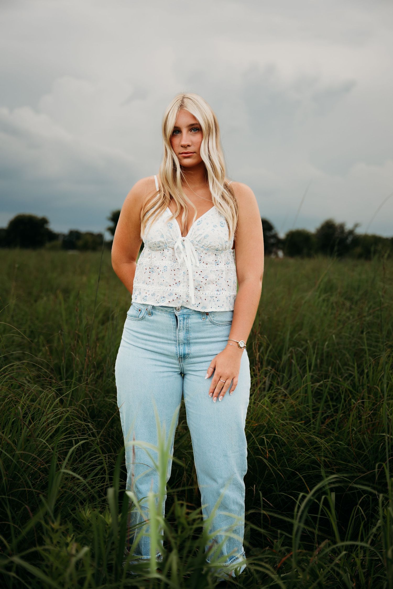 Casual summer outfit featuring a white lace camisole top and light wash jeans in an outdoor field setting.