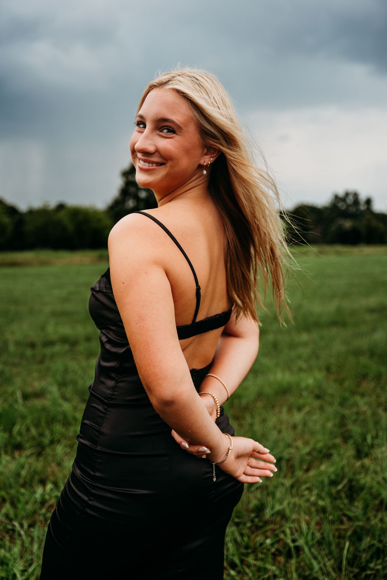 Person with flowing blonde hair in black dress dancing joyfully in a summer meadow.