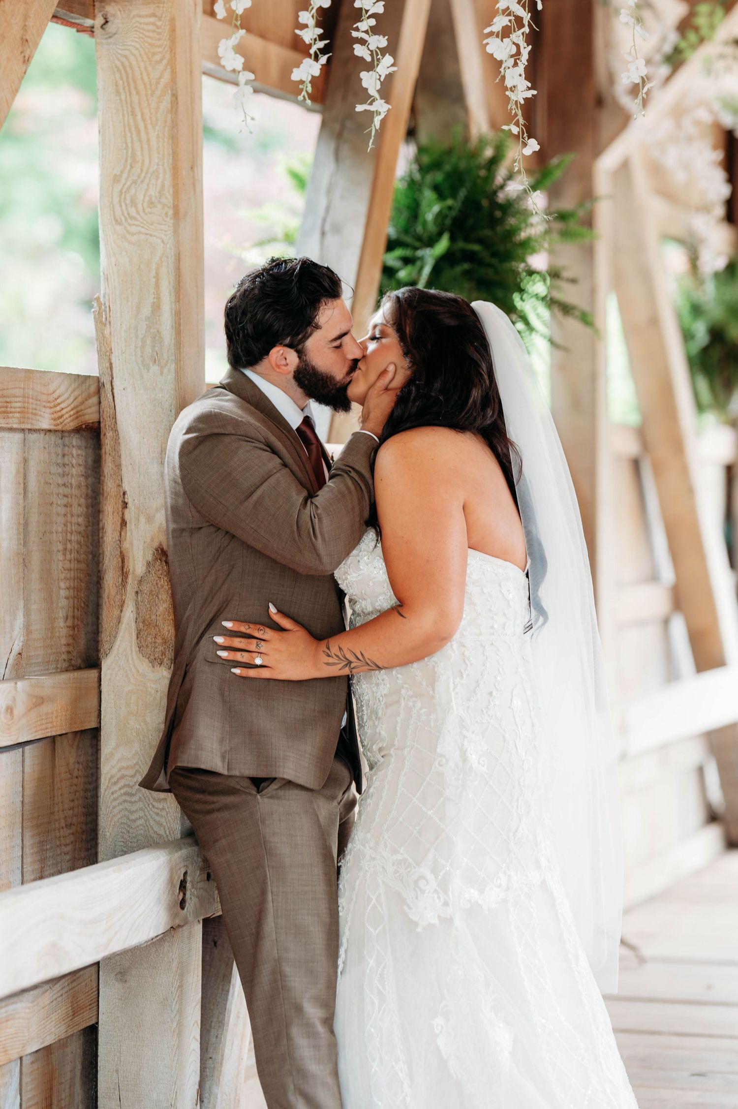 Bride and groom share a romantic kiss under floral decorations in a rustic wooden venue.
