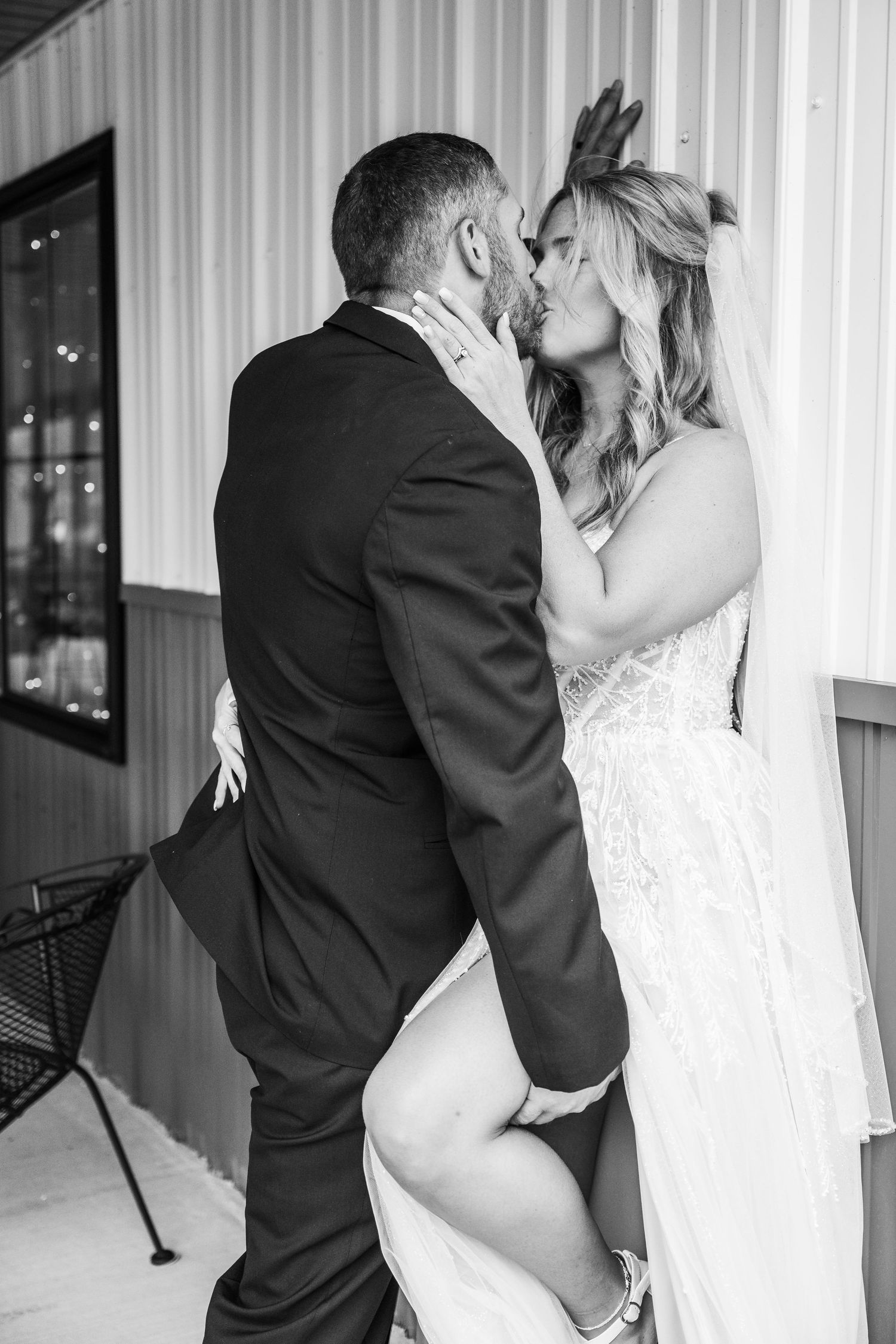 Black and white photo of newlyweds sharing a passionate kiss against a striped wall.
