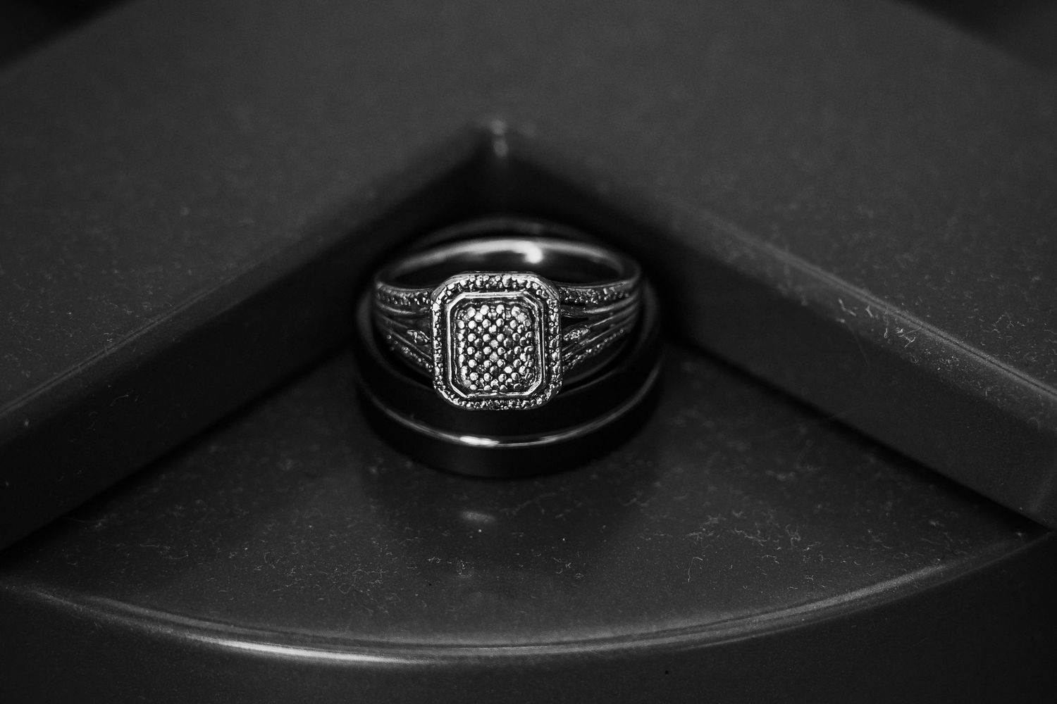 A black and white macro shot of an ornate silver ring with diamond setting resting in a dark corner.