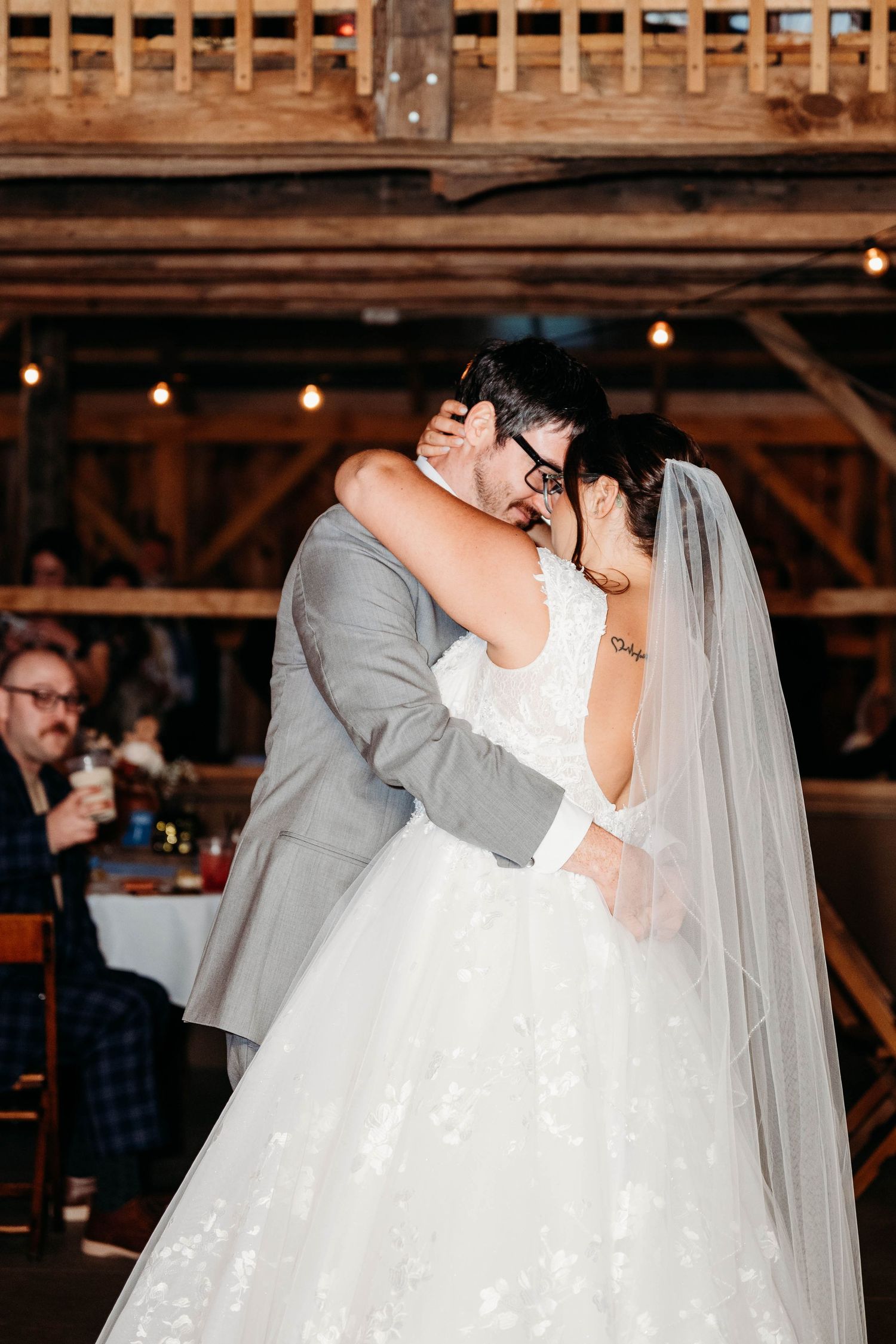 A couple shares their first dance at a rustic barn wedding reception with string lights overhead.
