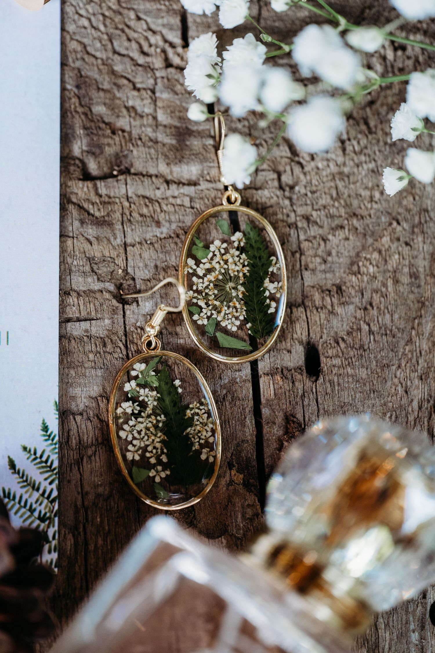 Vintage gold-rimmed sunglasses reflecting delicate white flowers against a rustic wooden background.
