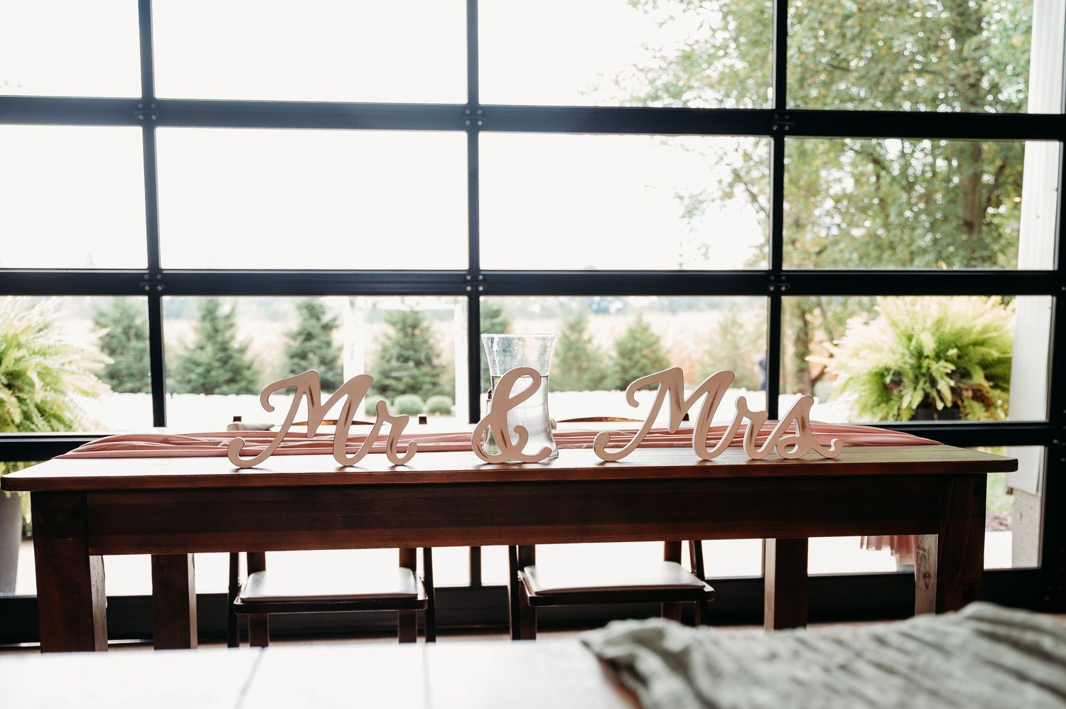 Modern office space with long wooden tables and glass walls overlooking a bright outdoor area.