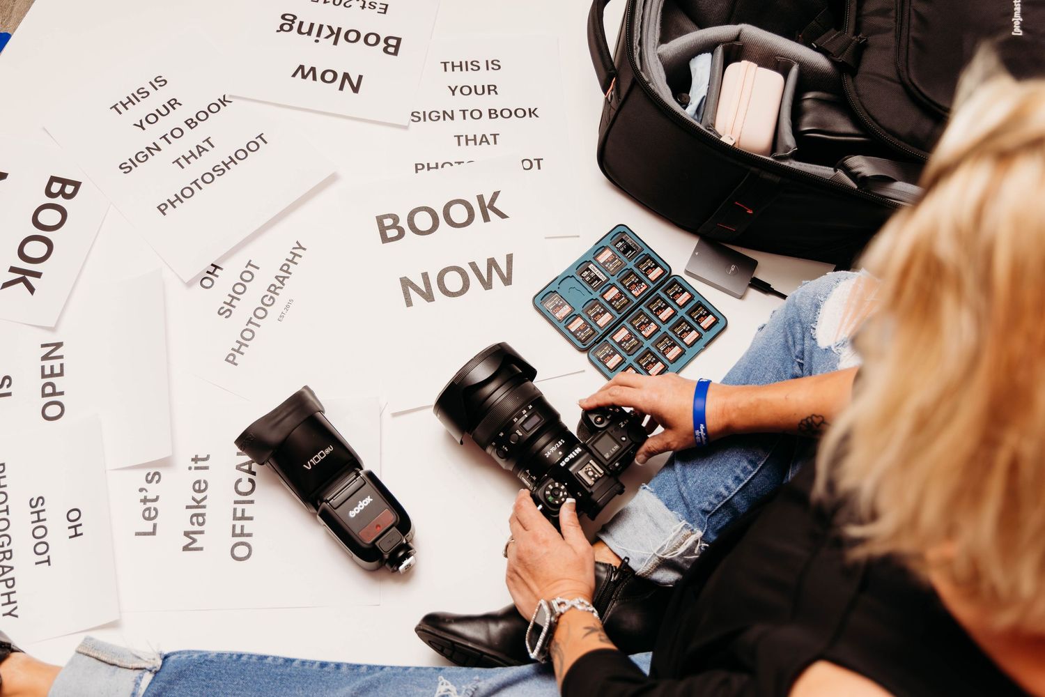 A person sitting with a camera and papers showing 'BOOK NOW' text while planning photography appointments.