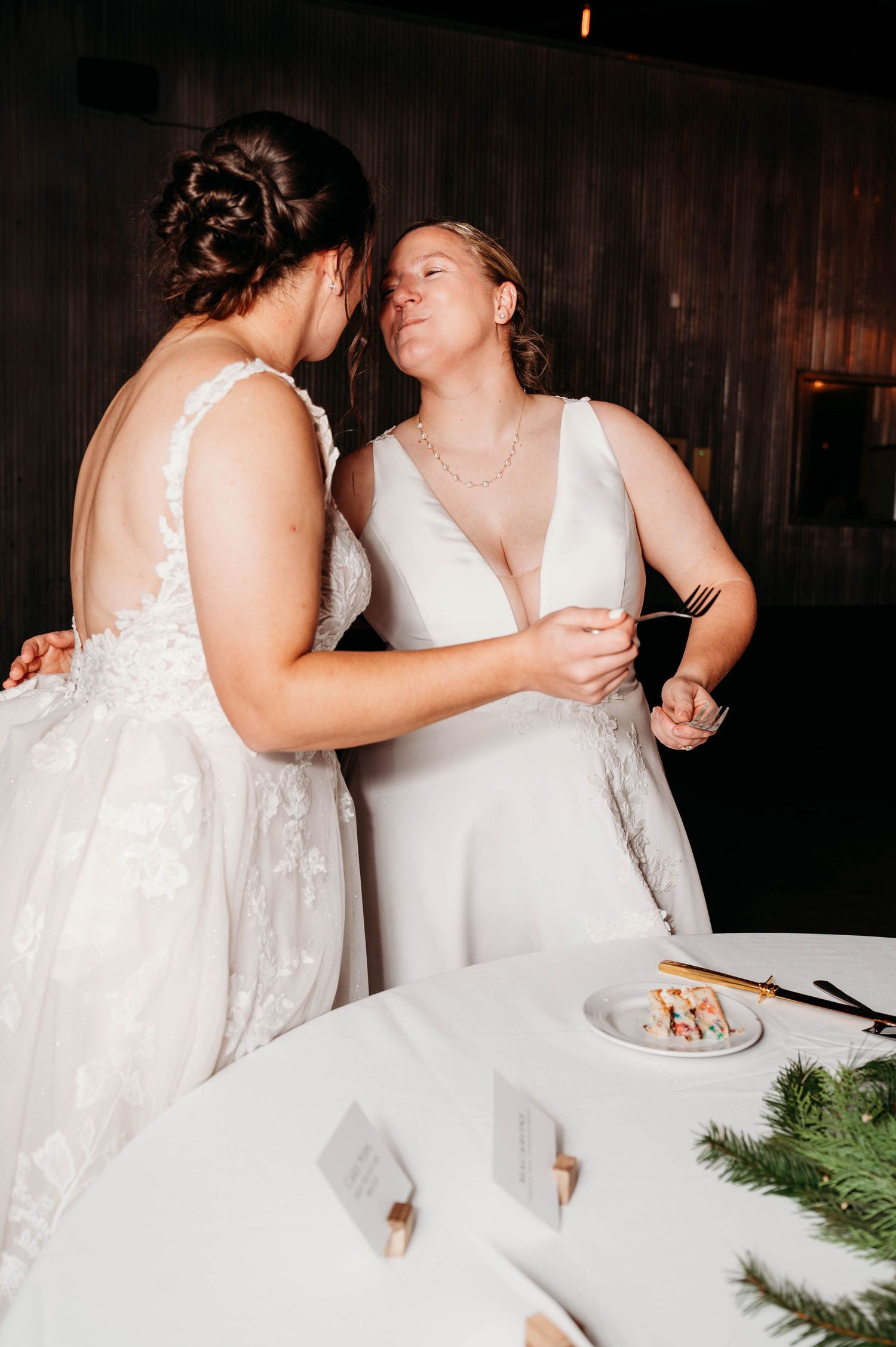 Wedding couple sharing cake at reception table decorated with greenery.
