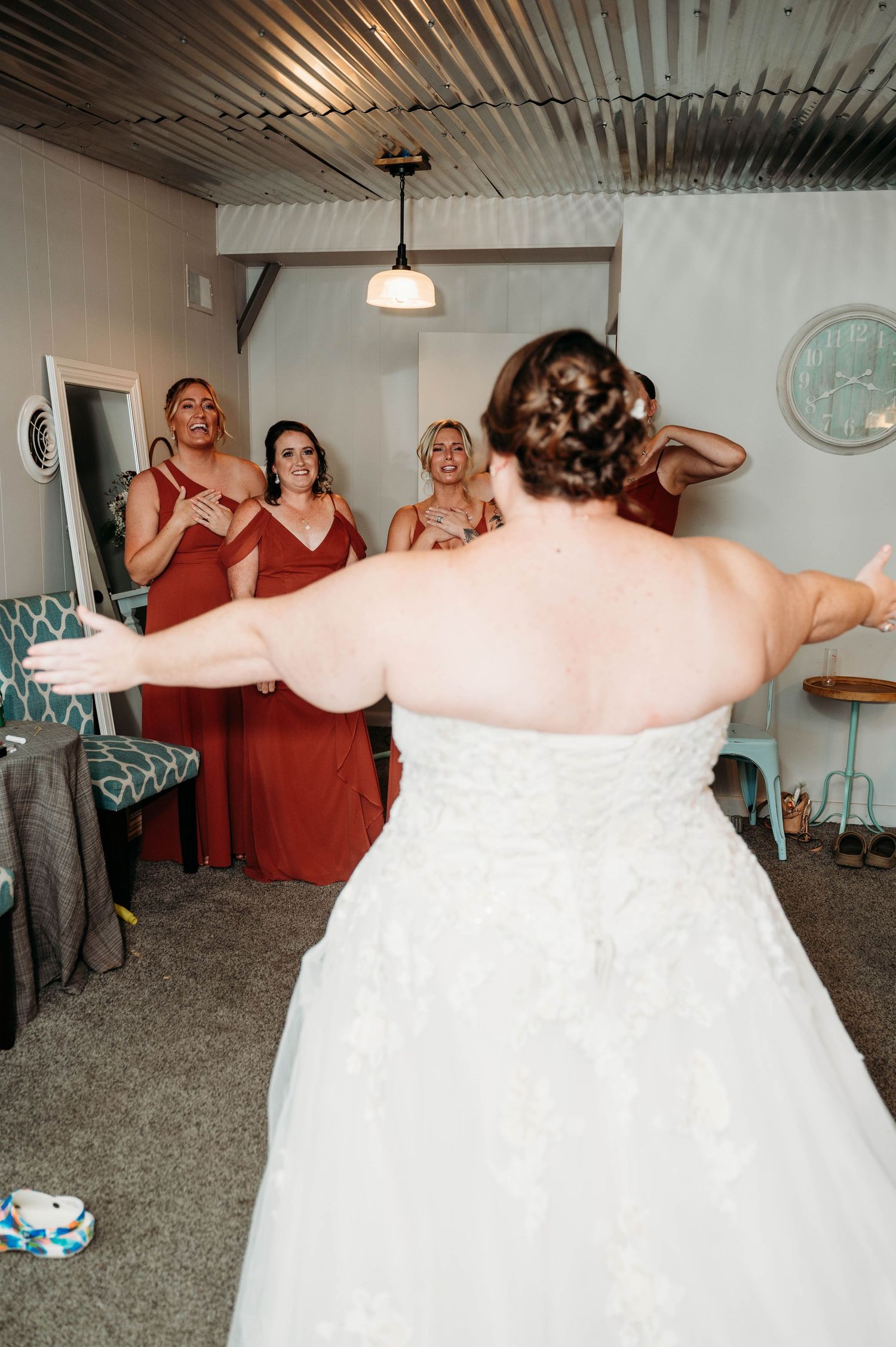 Wedding party in red bridesmaid dresses and white wedding gown posing playfully in a rustic room.