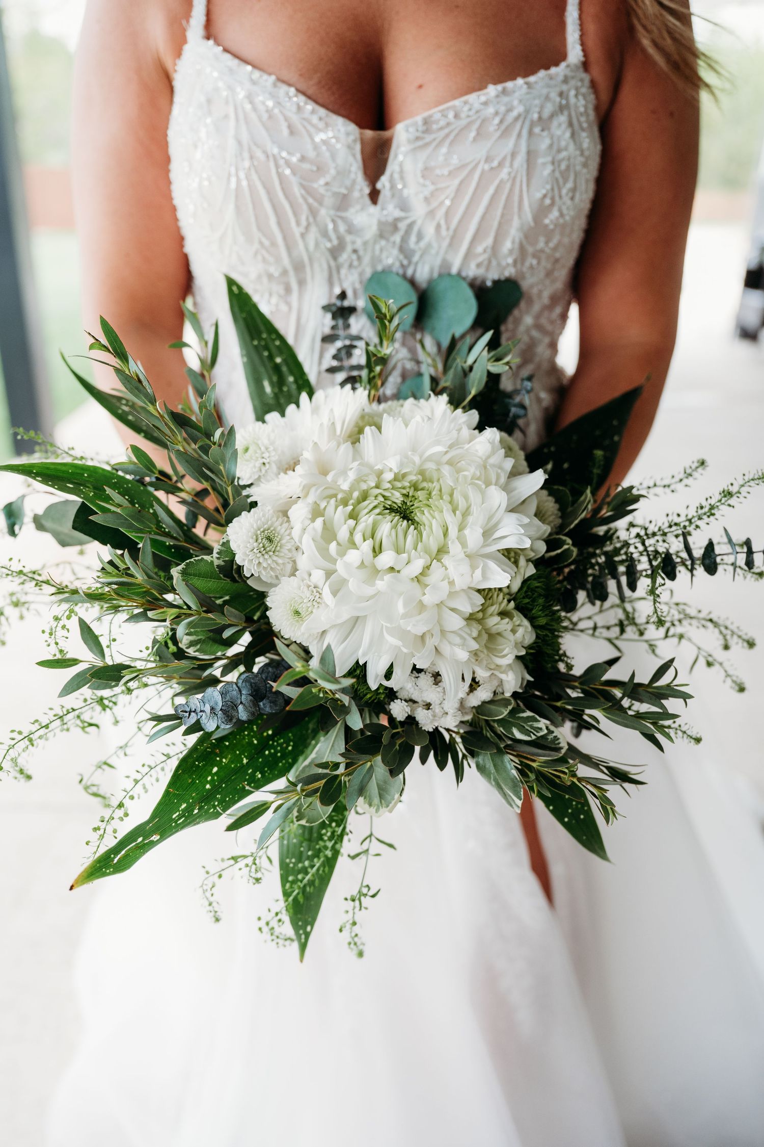 Bride in white beaded gown holding elegant bouquet of white dahlias and lush greenery.