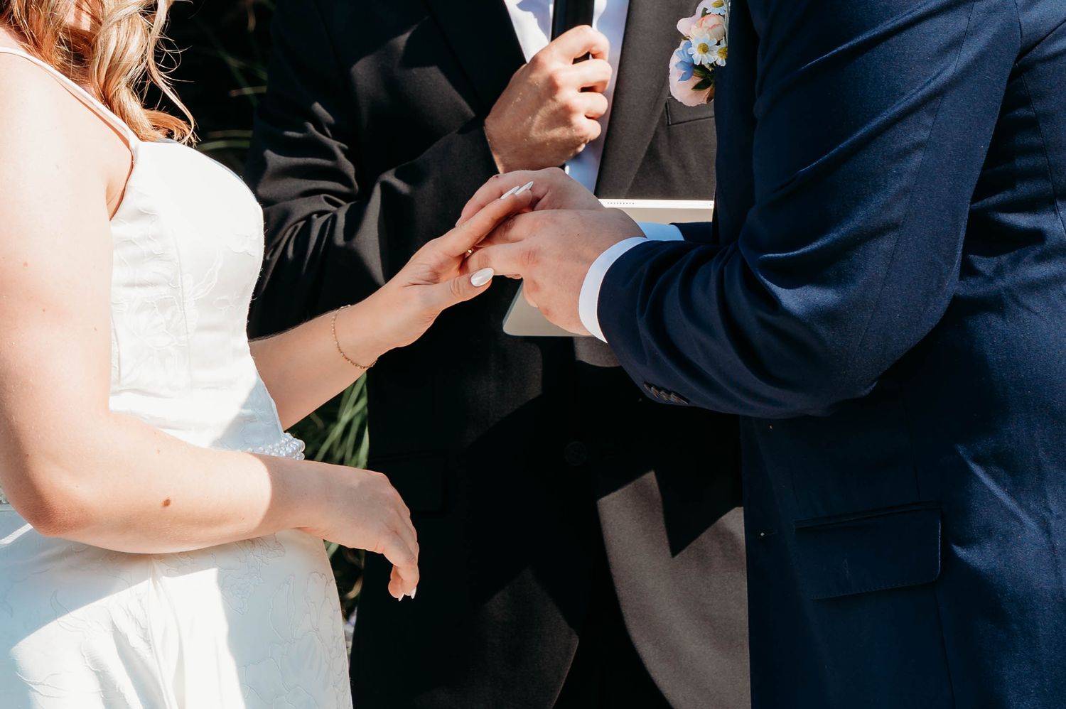 Groom placing a wedding ring on brides finger during outdoor ceremony.