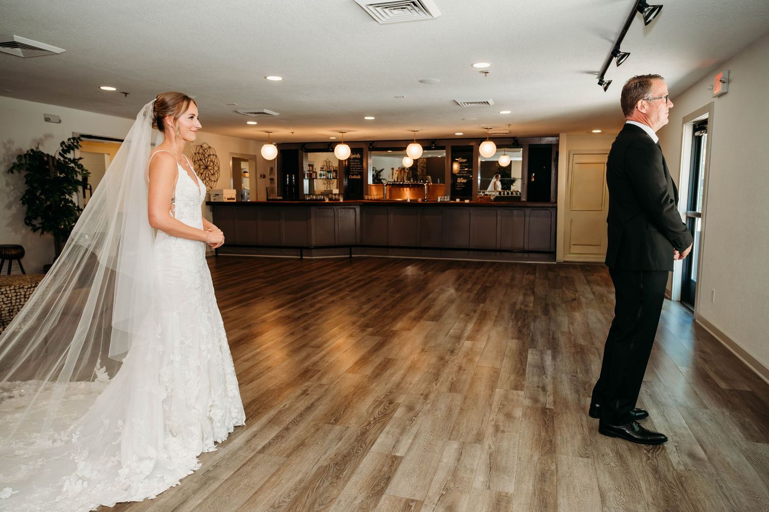 Bride in white lace gown and veil shares first look moment with groom in tuxedo in elegant venue.