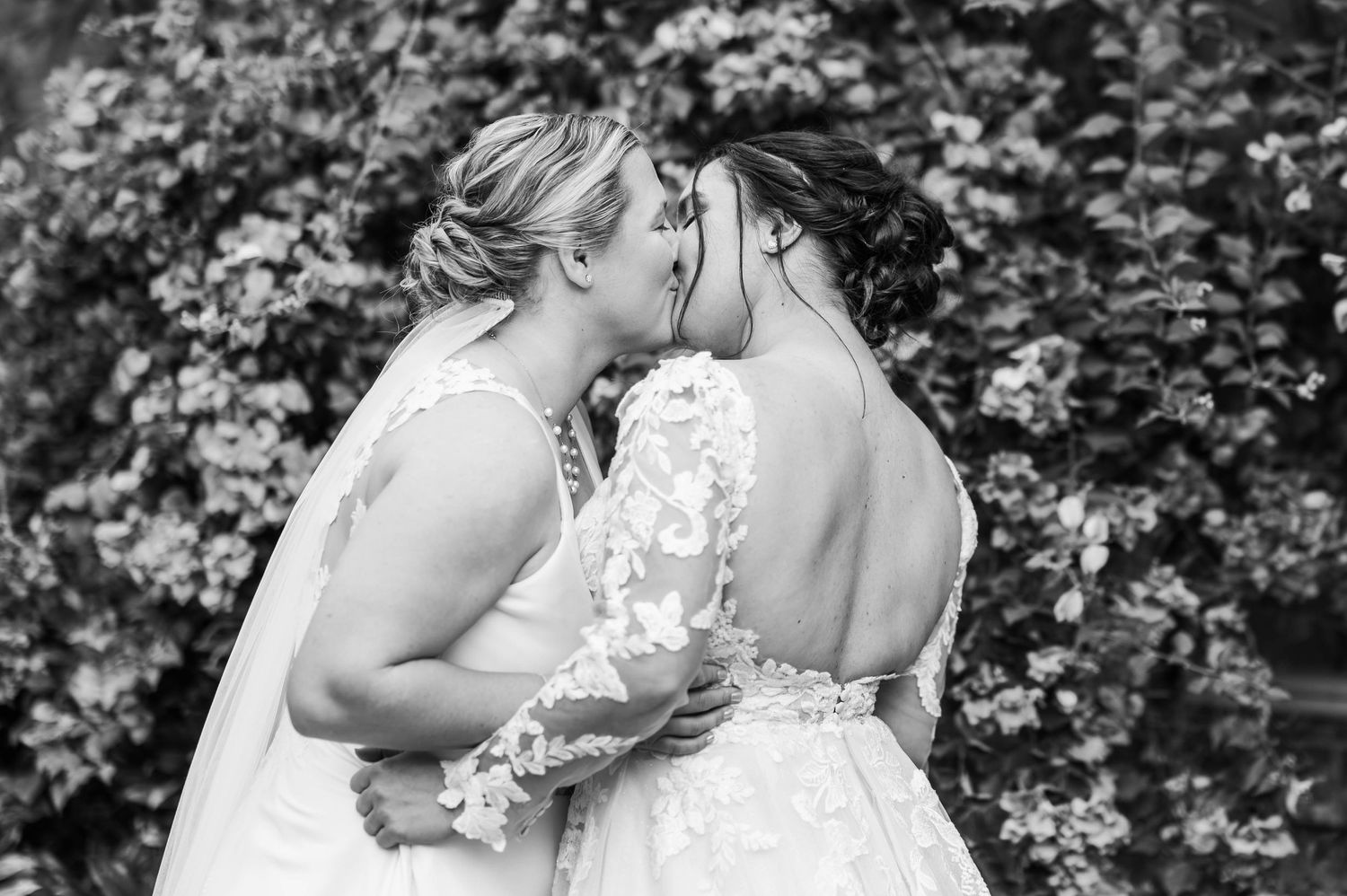 A romantic black and white wedding portrait shows a tender moment between newlyweds in a garden setting.