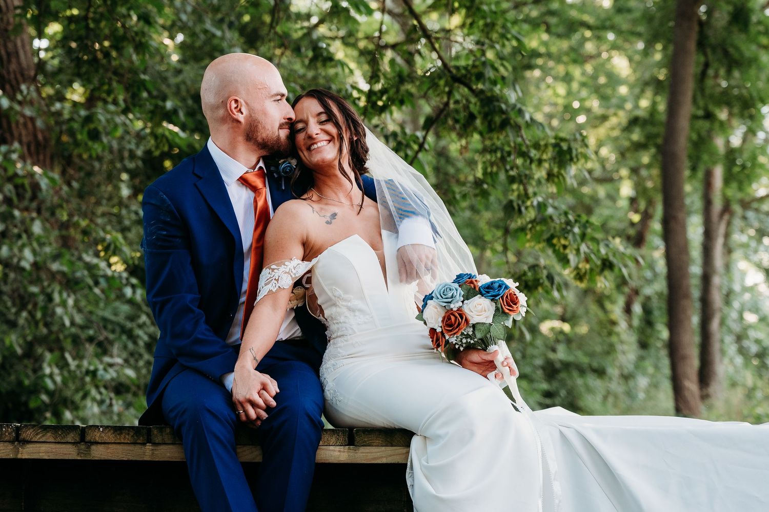 Newlyweds share romantic kisses in an outdoor wooded setting while wearing traditional wedding attire.