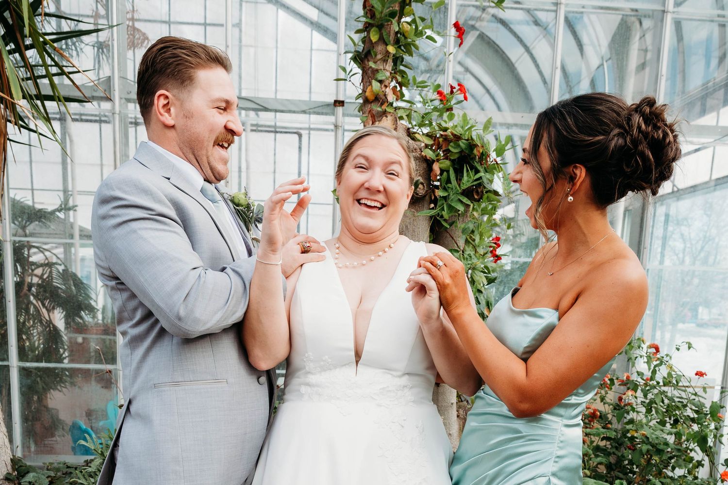 Wedding party sharing joyful laughter in a bright greenhouse setting.