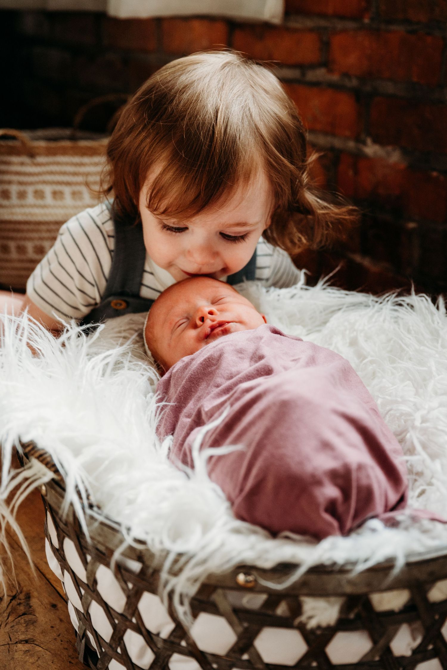 A cozy scene with a small child resting on white feathery bedding in a rustic setting with brick walls.