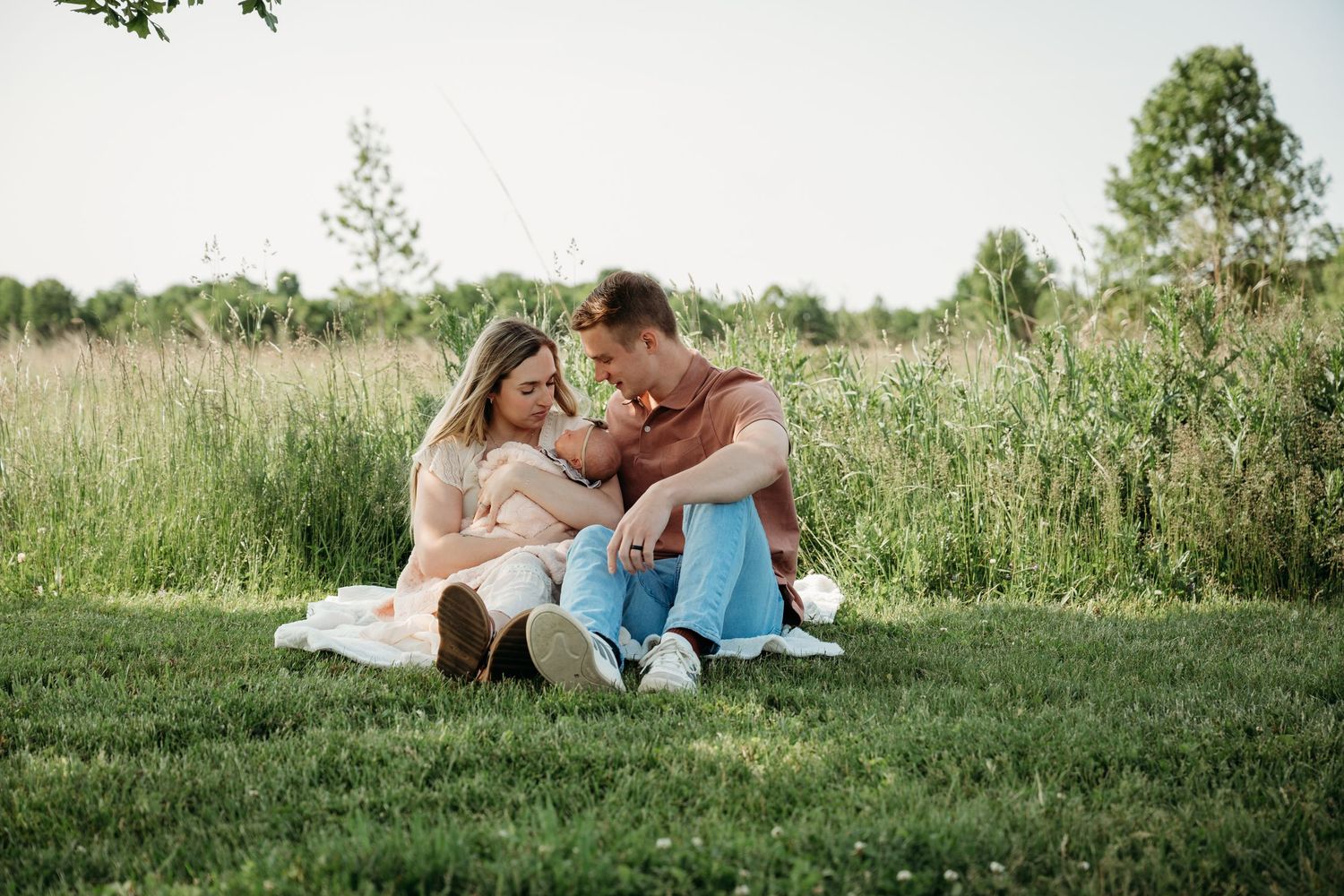 A couple sits together in a grassy meadow on a sunny summer afternoon.