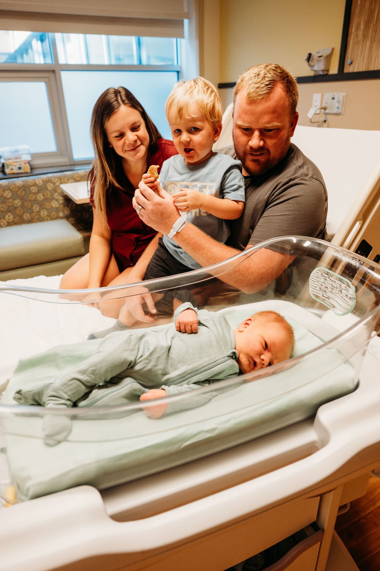 Family members gather around an infant on a changing table in a medical setting, showing tender moments of interaction.