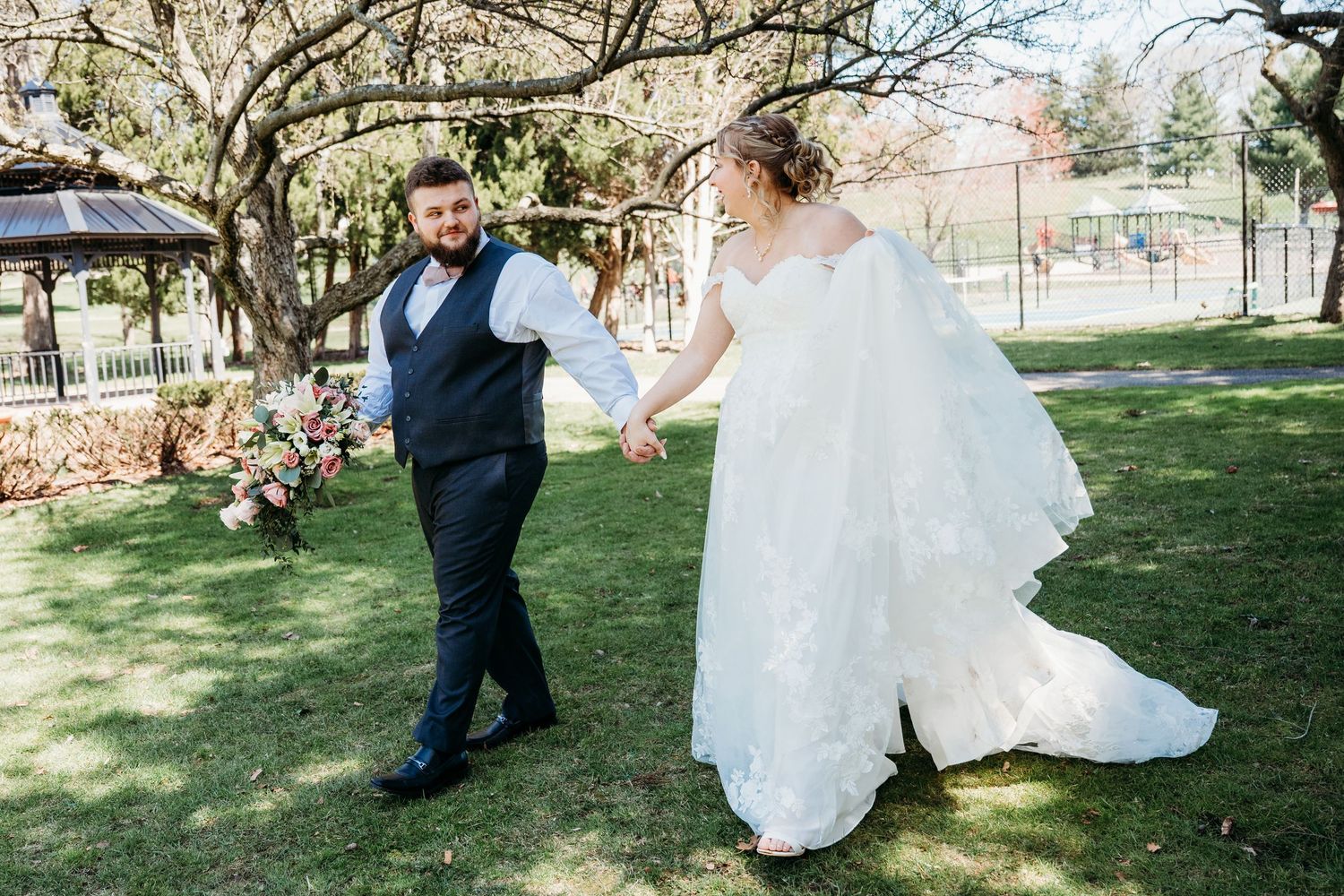A joyful couple dances together on a sunny spring day in a garden setting with trees and flowers in the background.