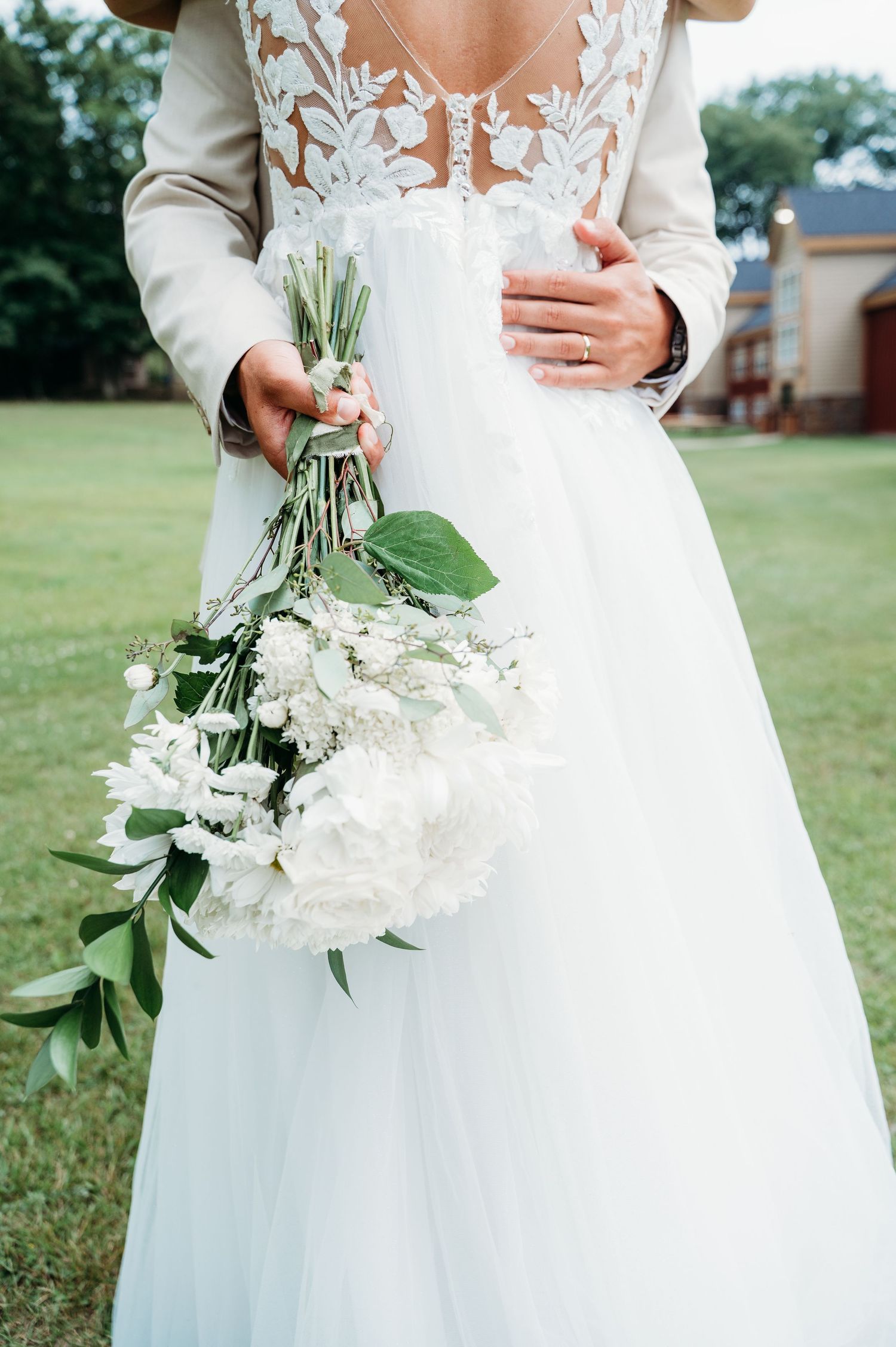 Close-up view of a wedding bouquet with white flowers and greenery held against a flowing white wedding gown.