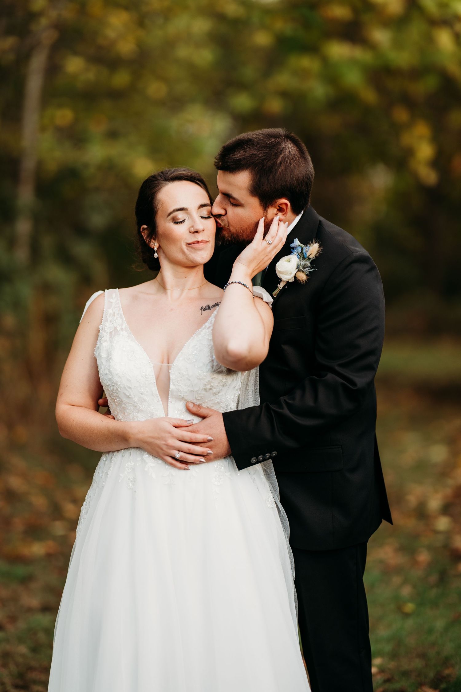 A couple shares an intimate moment during their outdoor wedding photoshoot in a wooded setting with autumn colors.