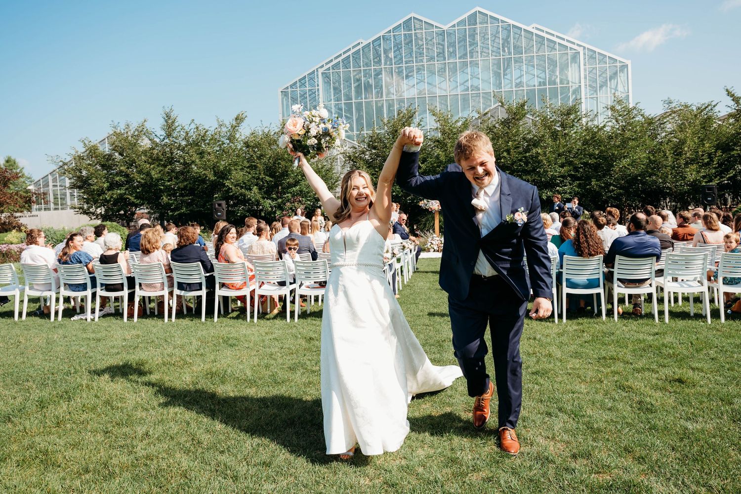 Newlyweds celebrate joyfully as they walk back down the aisle after outdoor wedding ceremony.