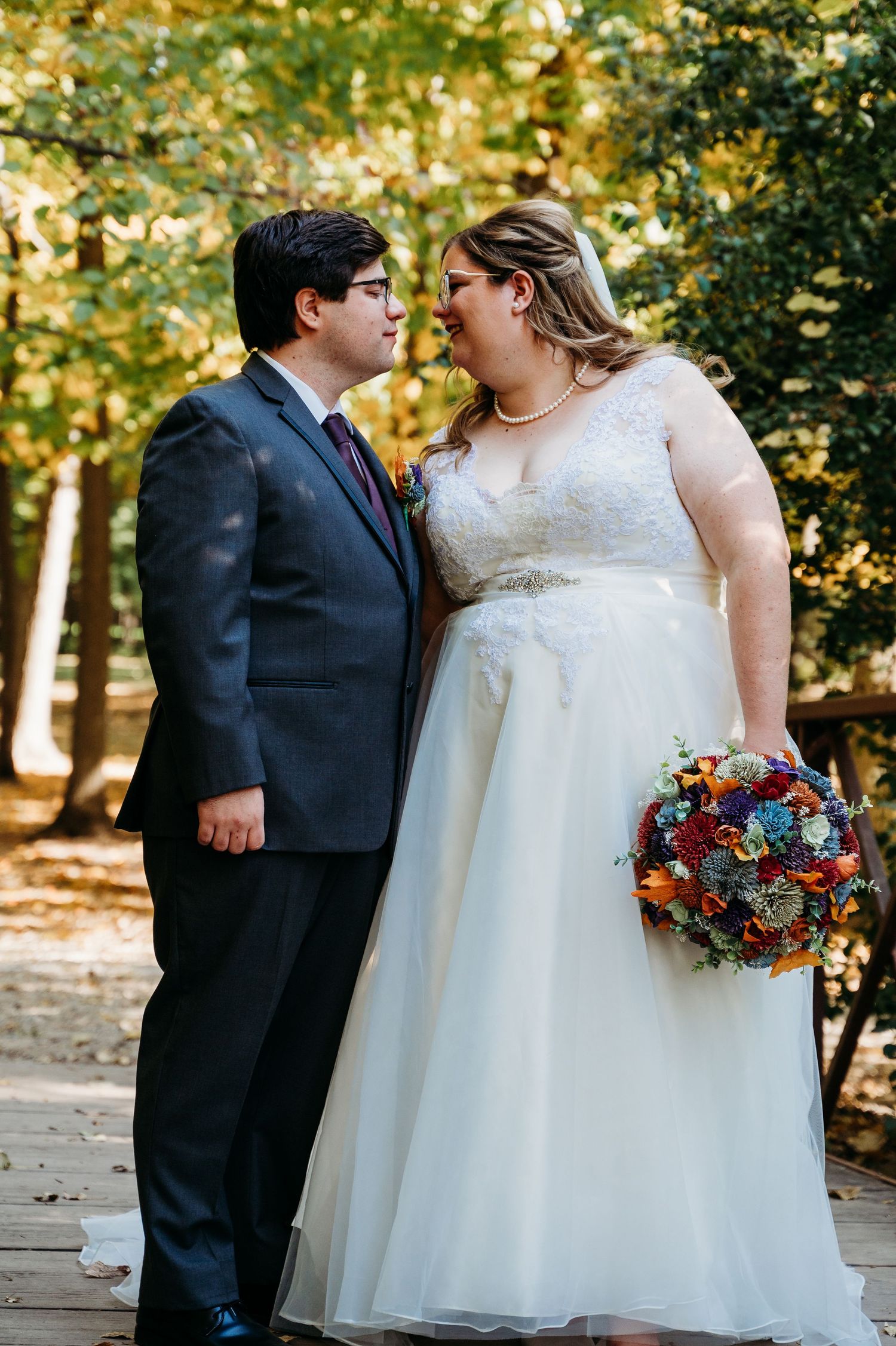 A joyful couple shares a moment together in the outdoors, with the bride holding a colorful fall bouquet.
