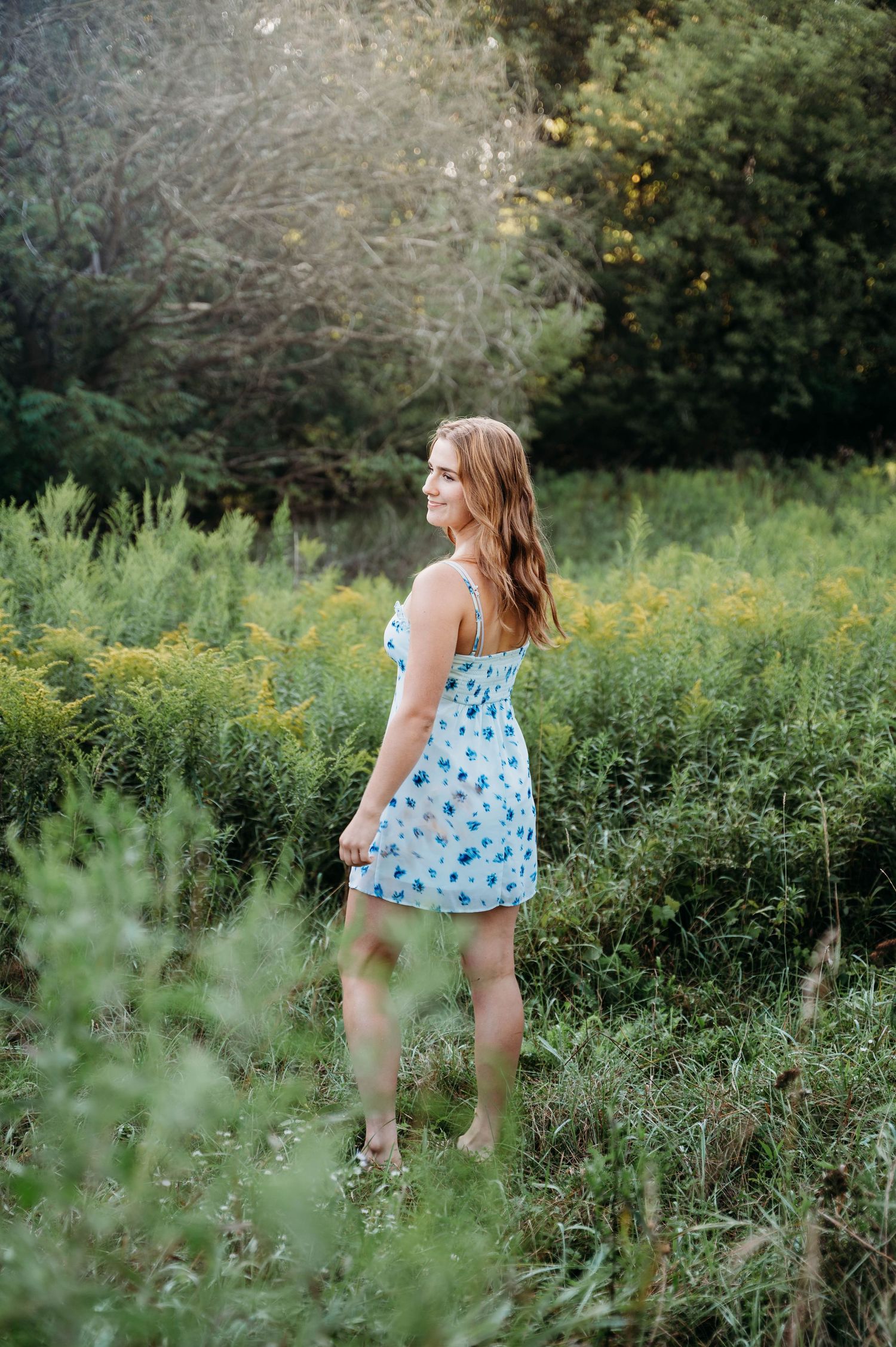 A person in a blue floral sundress stands among wildflowers and tall grass on a sunny summer afternoon.