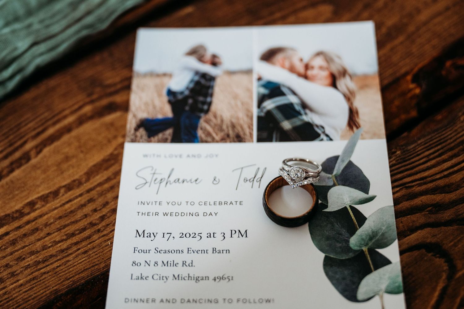 Wedding invitation with photos, eucalyptus leaves and engagement ring arranged on wooden surface.