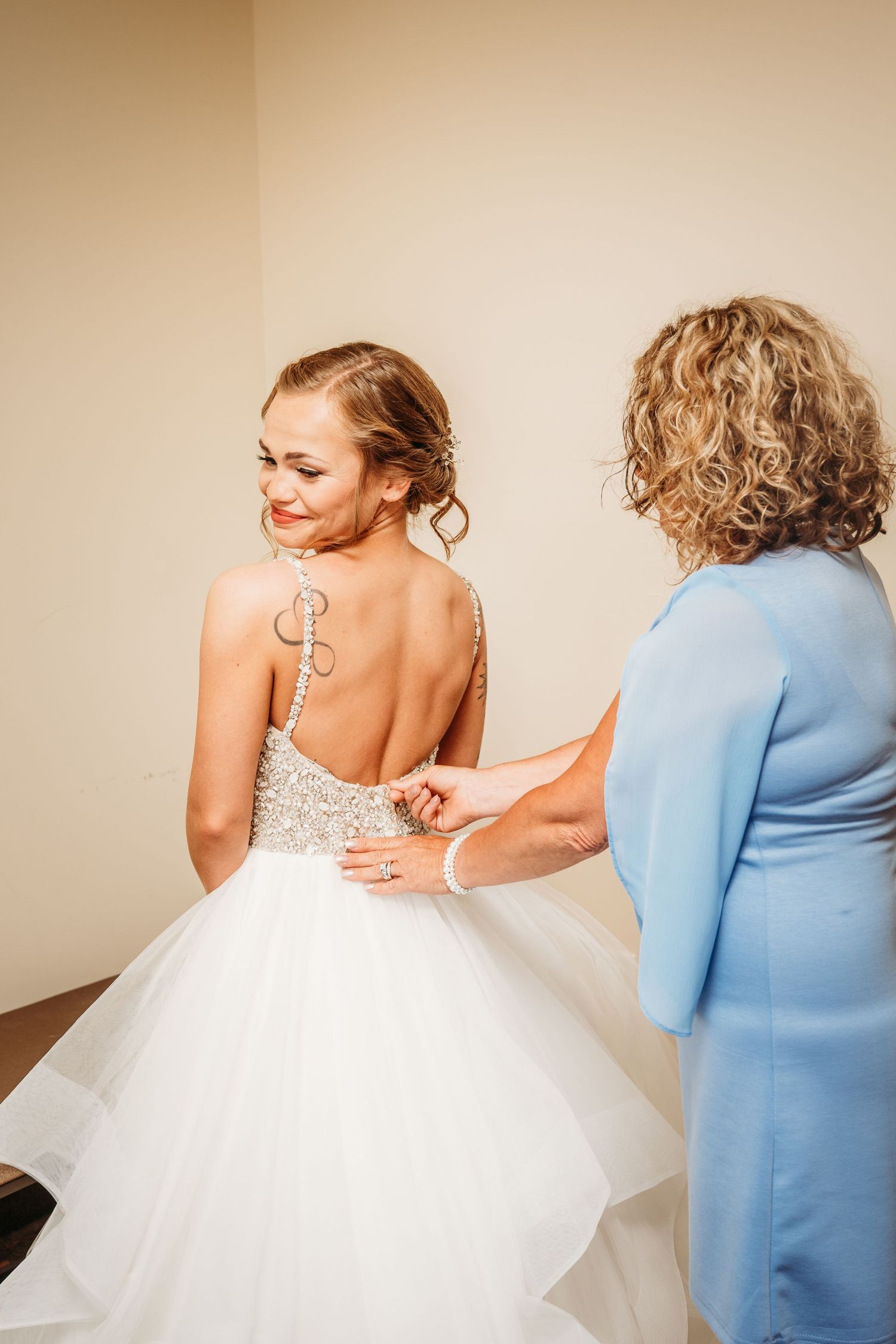 Someone helps adjust the corset back of a white tulle wedding gown dress during bridal preparations.