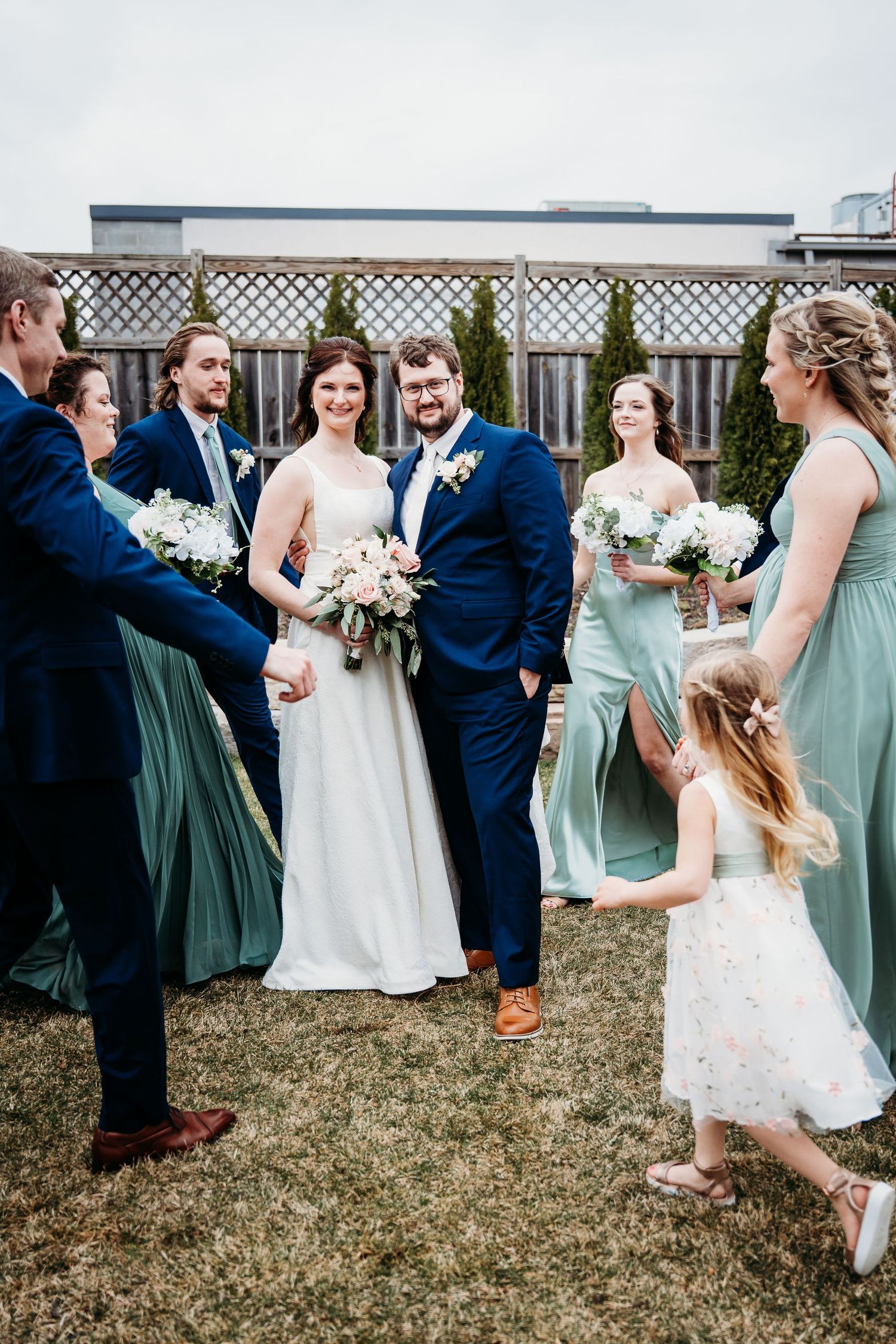 Wedding party in navy and mint green attire gather on lawn for formal photos with bridesmaids and flower girl.