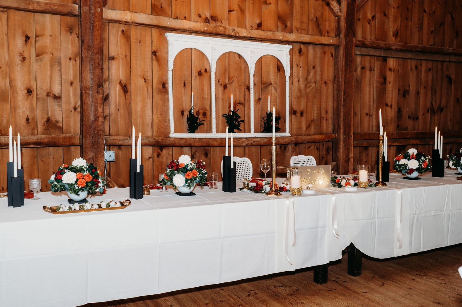 Rustic wooden barn interior with long tables arranged for banquet seating and small lanterns lining the walls.