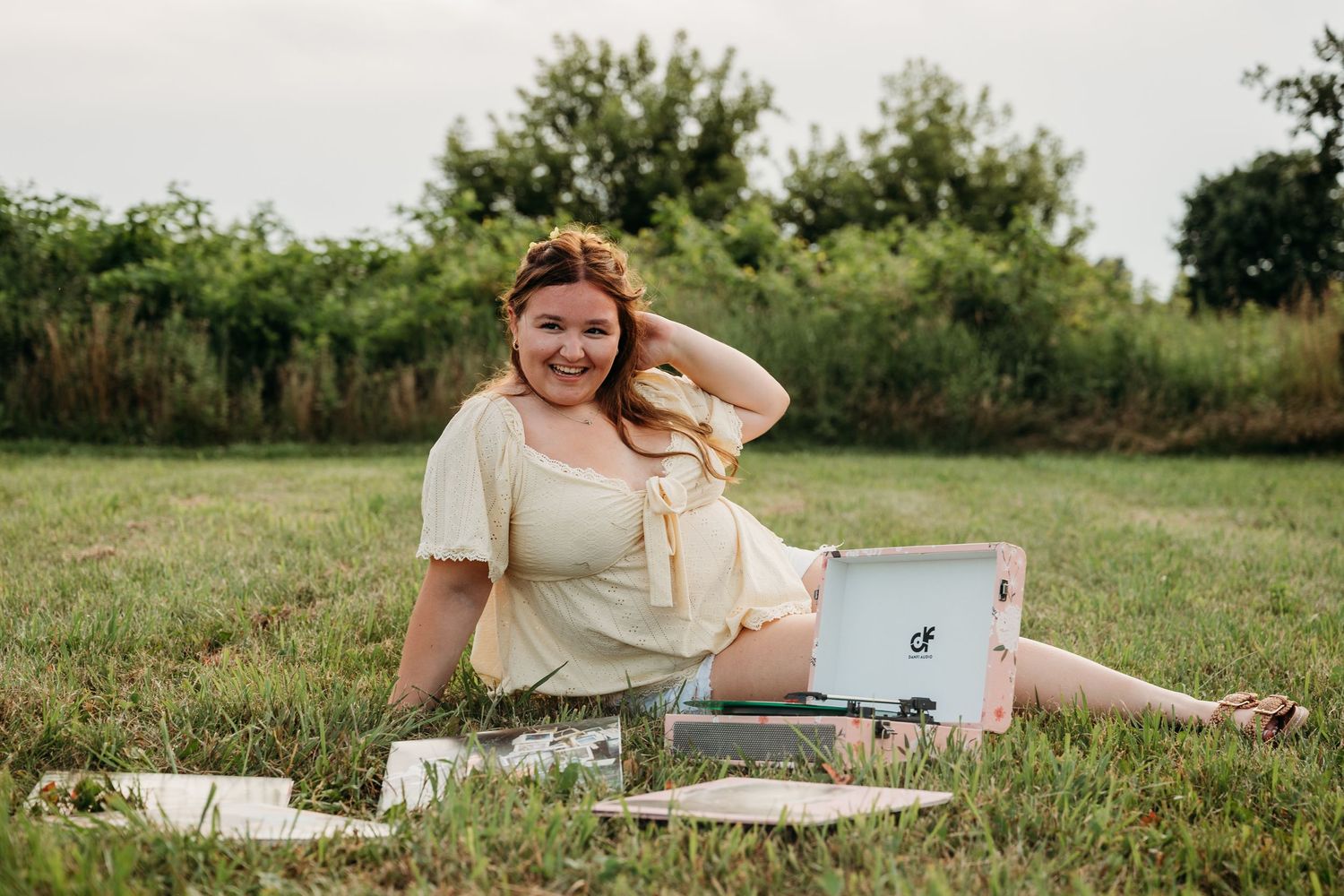 Someone sits and studies with notebooks and papers scattered on a blanket in a grassy outdoor setting.