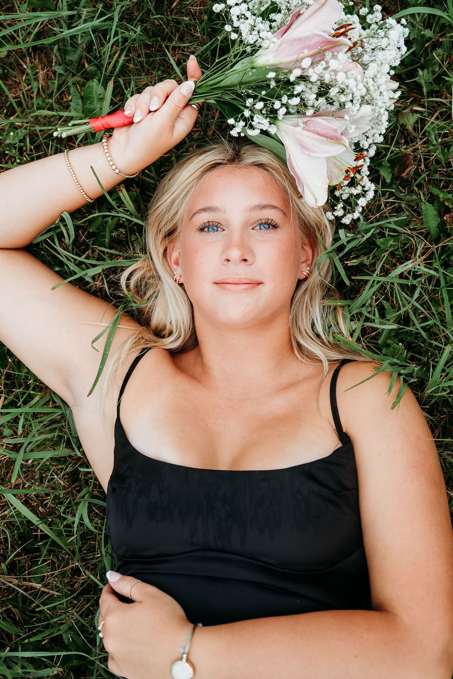 A person lying in grass wears a black dress with baby's breath flowers arranged around their head.