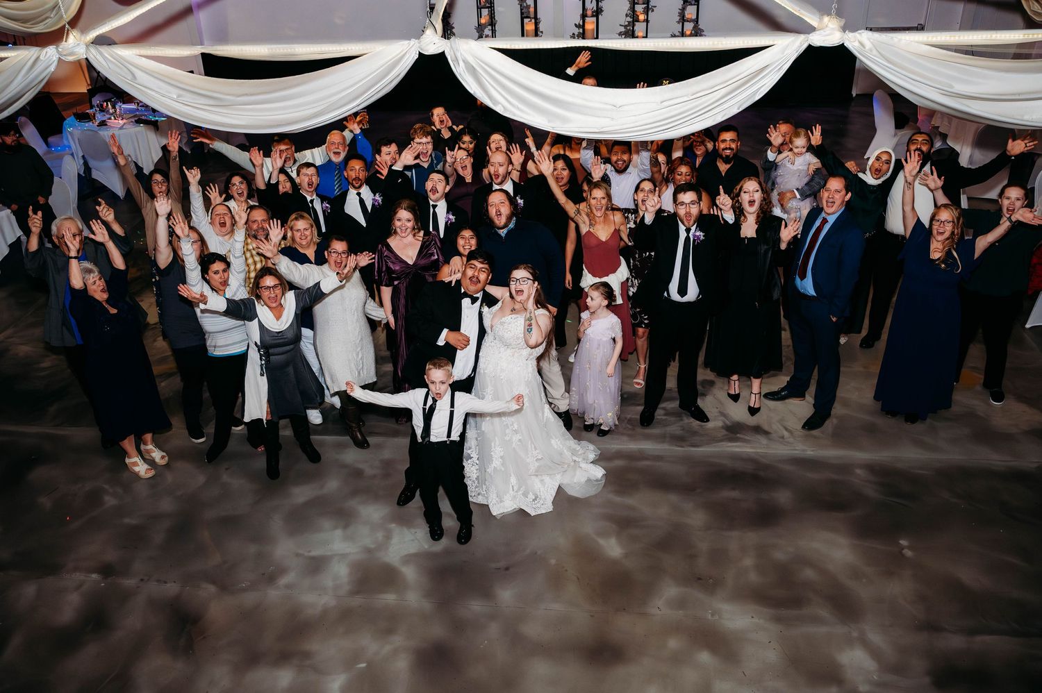 Bride and groom celebrate on dance floor surrounded by cheering wedding guests at elegant indoor reception. Wedding at Fountains Banquet Cen