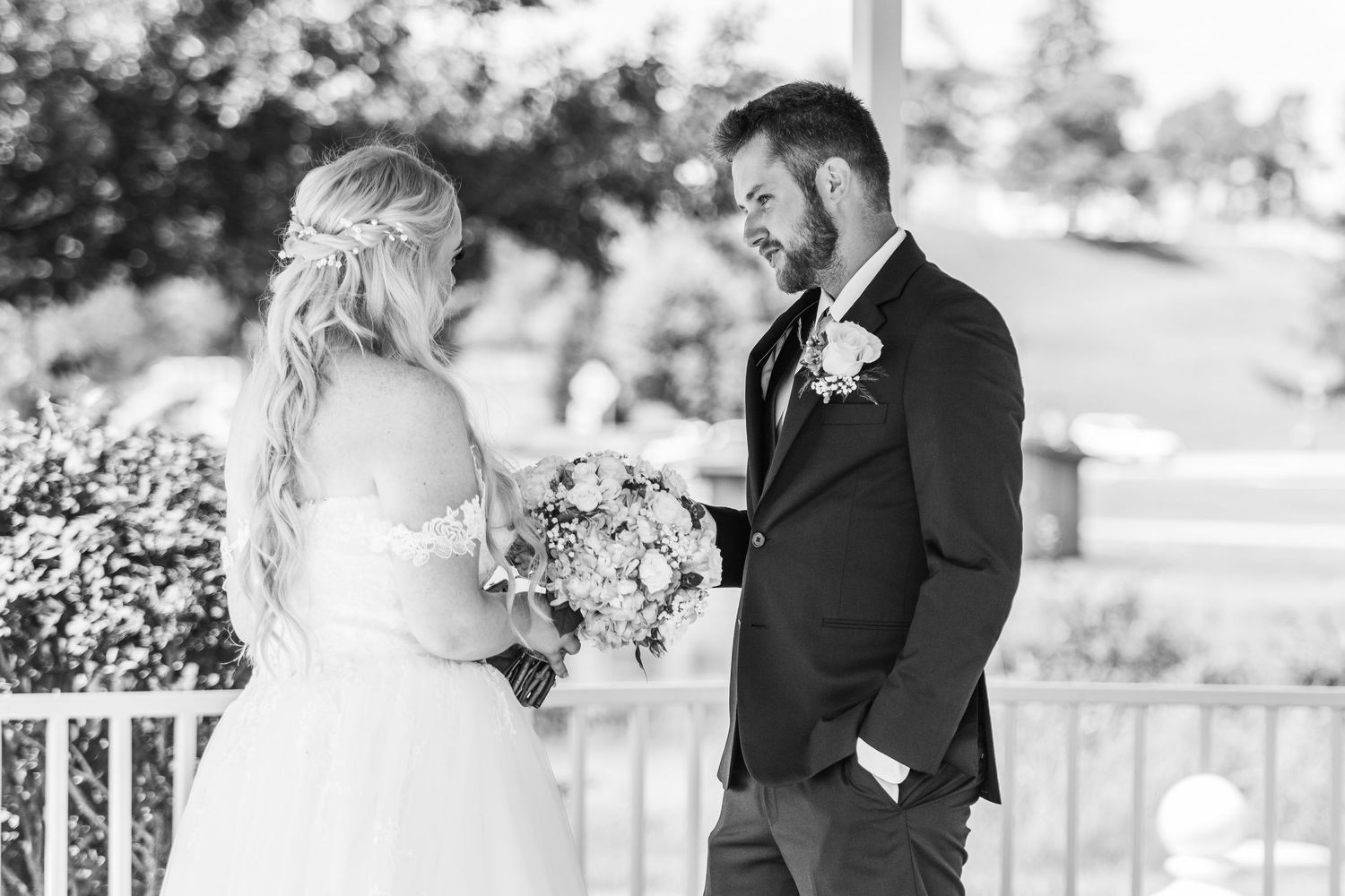 Black and white photo of a bride and groom sharing a first look moment on a porch during their wedding day.