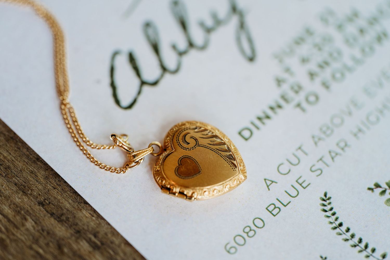Gold heart-shaped locket necklace resting on a wooden surface next to green text on paper.