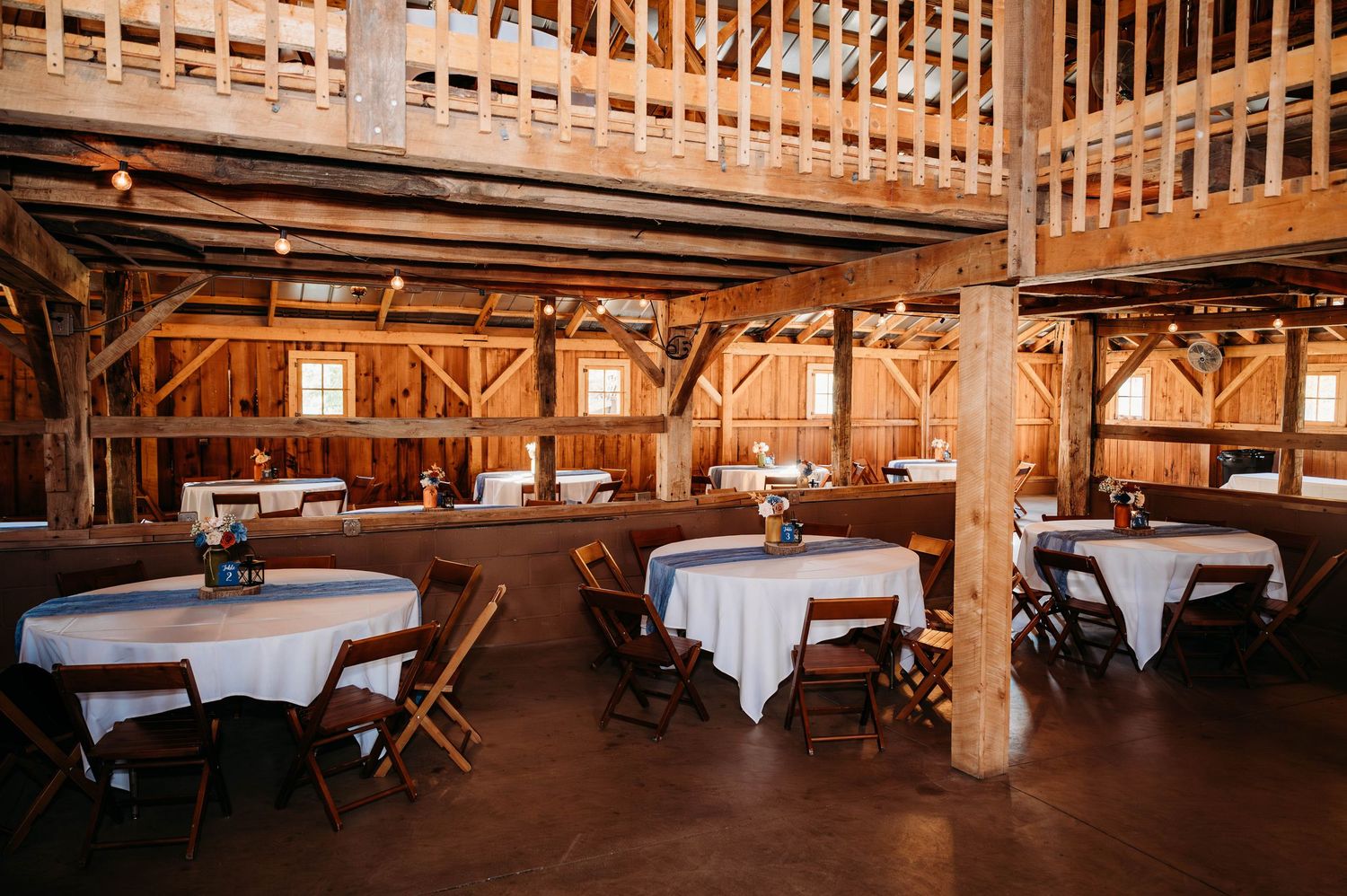 Rustic wooden barn interior set up for an elegant event with white tablecloths and exposed wooden beams throughout.