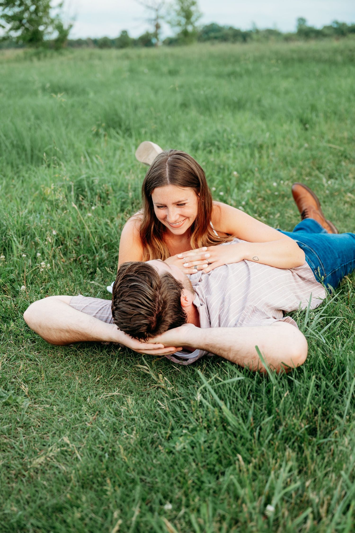 Happy couple relaxing on green grass field, woman smiling while man rests his head on her lap outdoors.