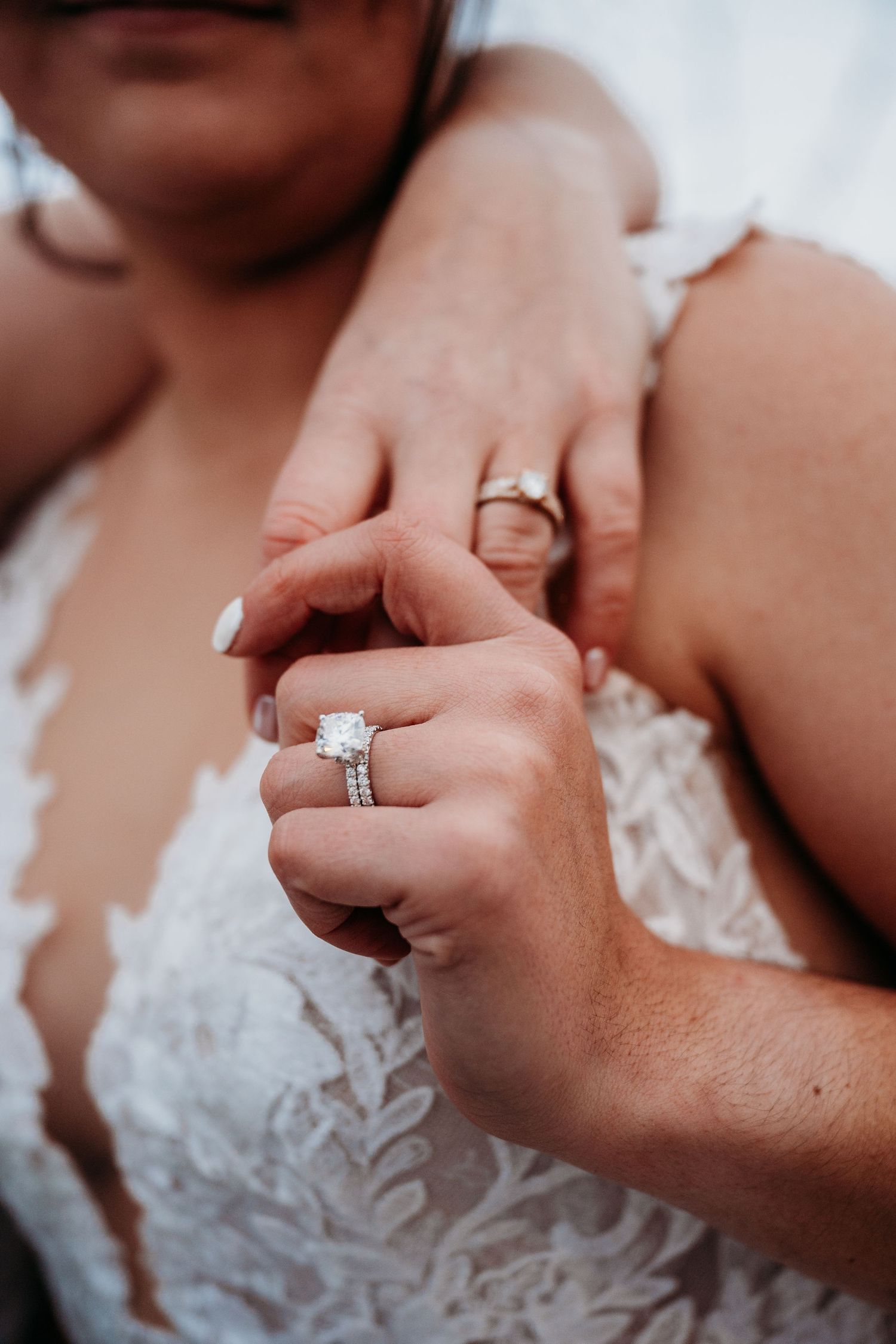 Close-up collage of hands showing engagement and wedding rings with white lace dress details.