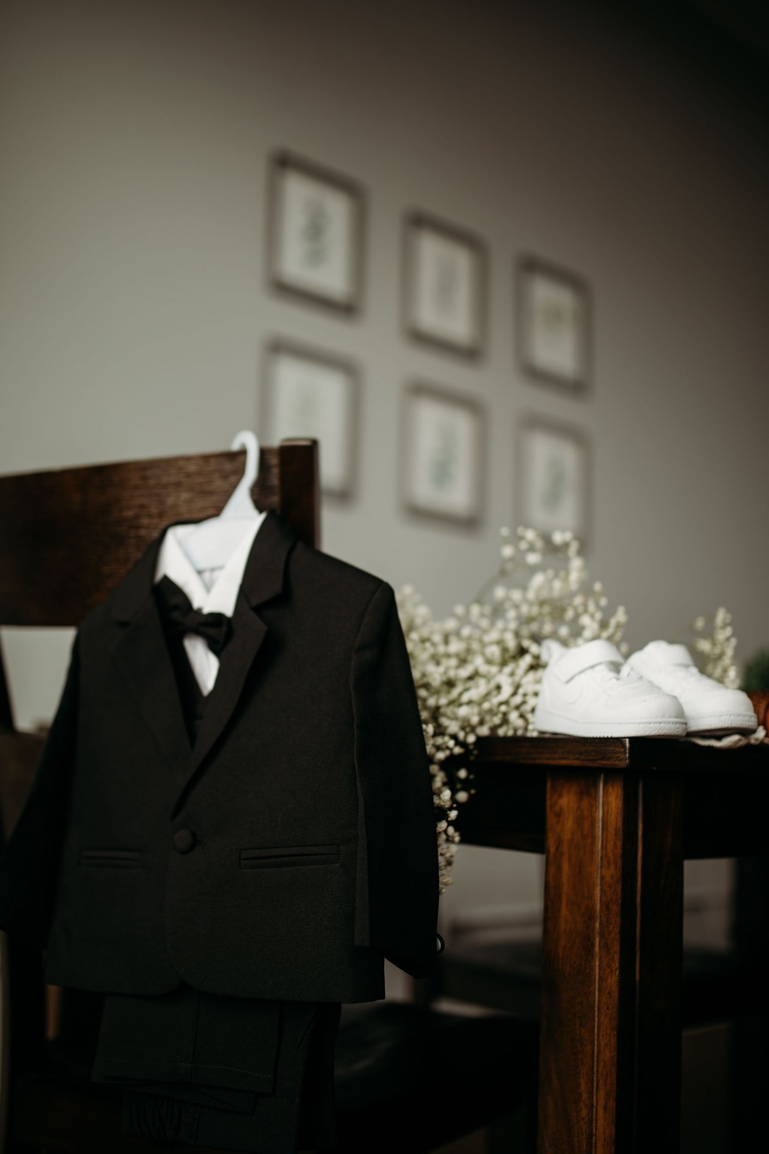 Wedding detail shot of black tuxedo and white dress shoes with baby's breath decoration.