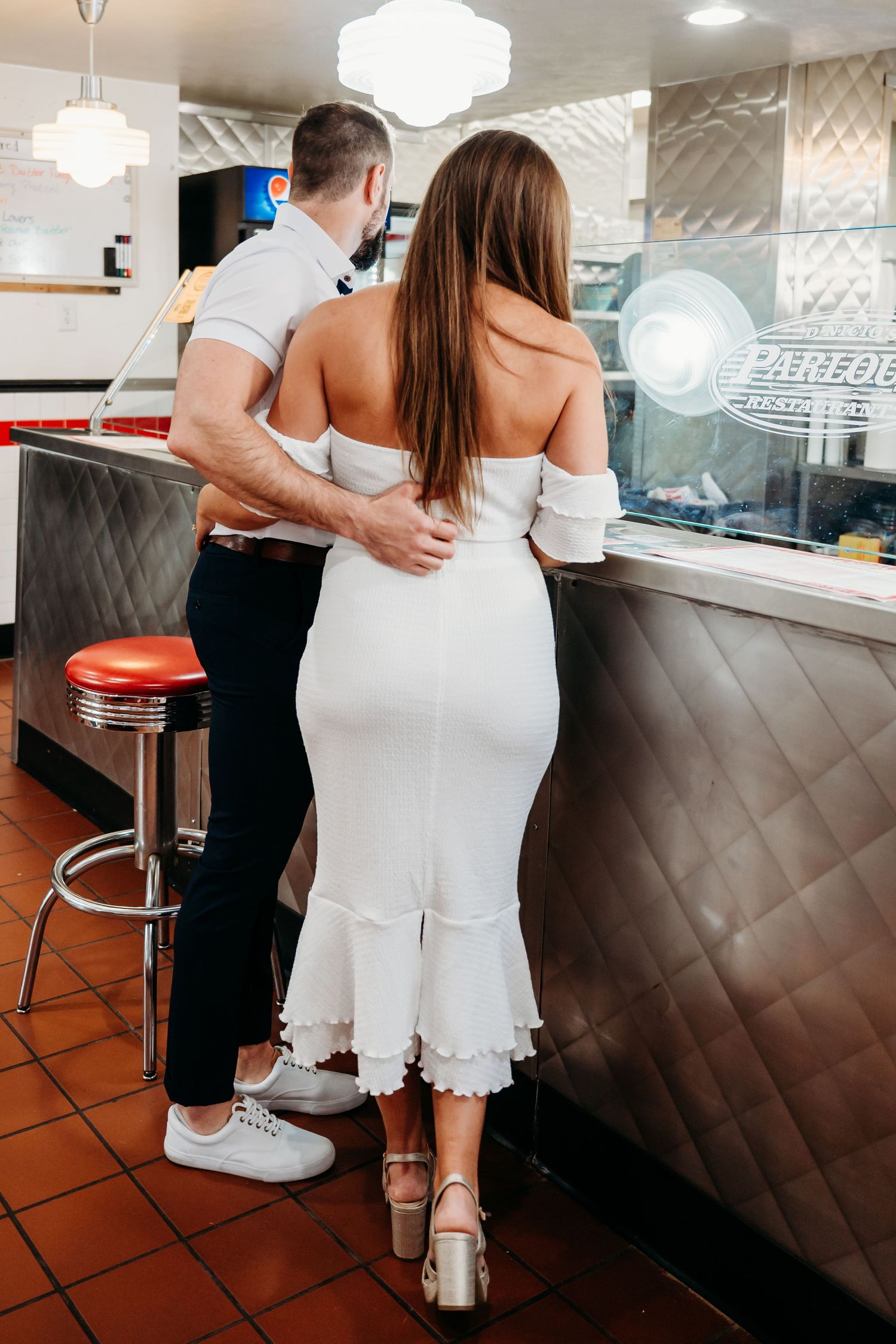 A couple in light-colored outfits sharing an intimate moment at a retro-style diner counter.