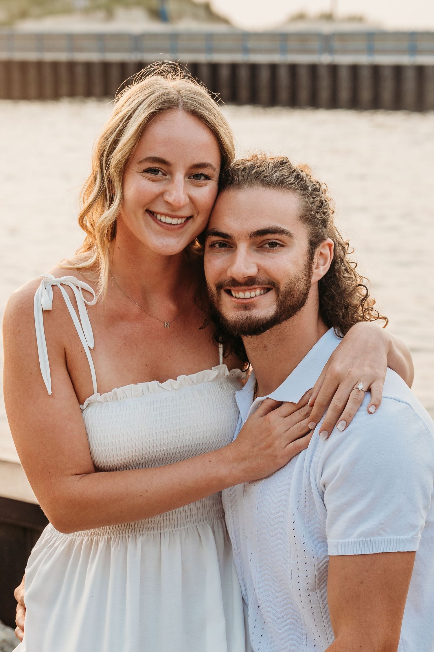 A romantic couple in white outfits embracing on the beach during golden hour.