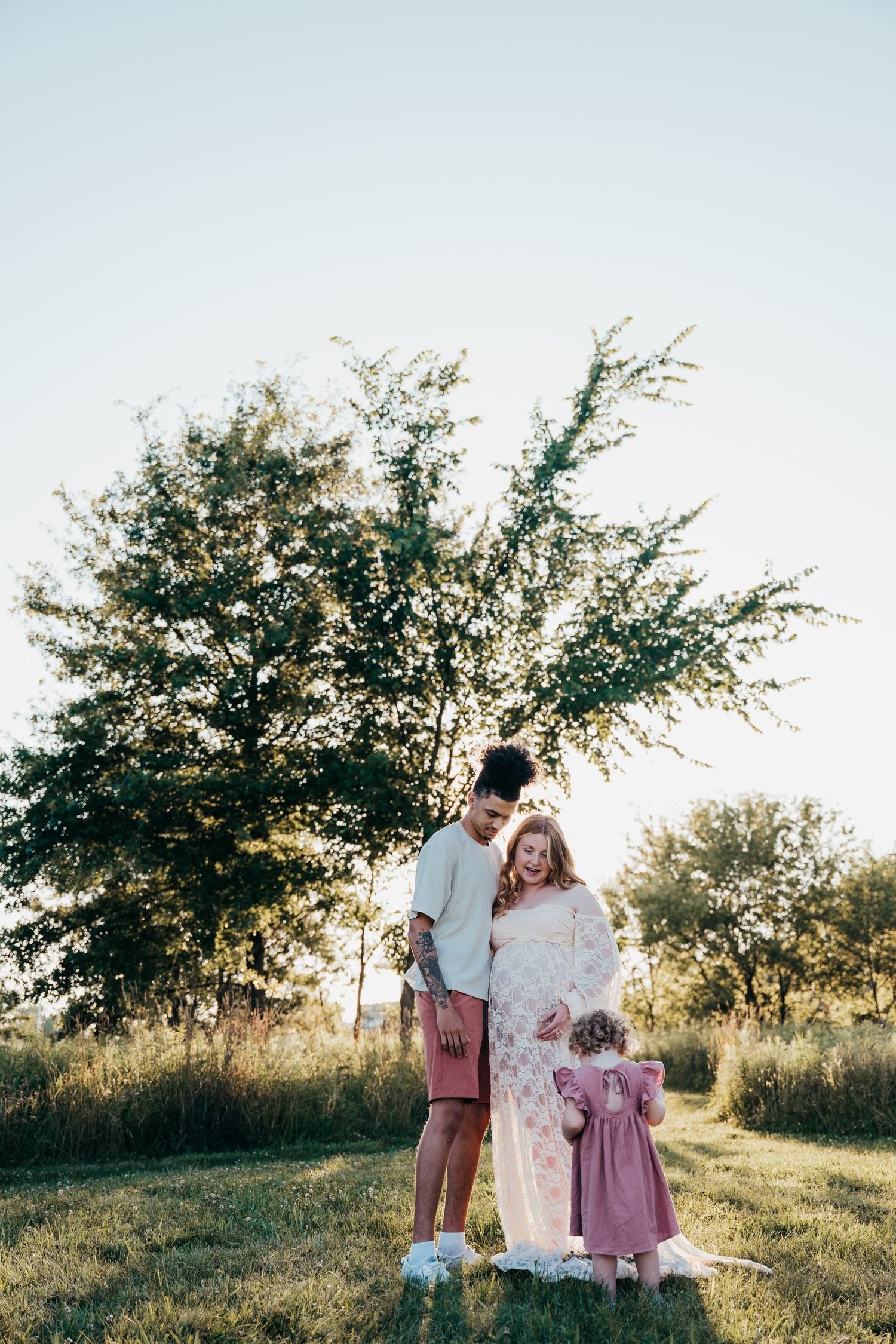 A group stands together in a sunlit grassy field during golden hour with trees in the background.