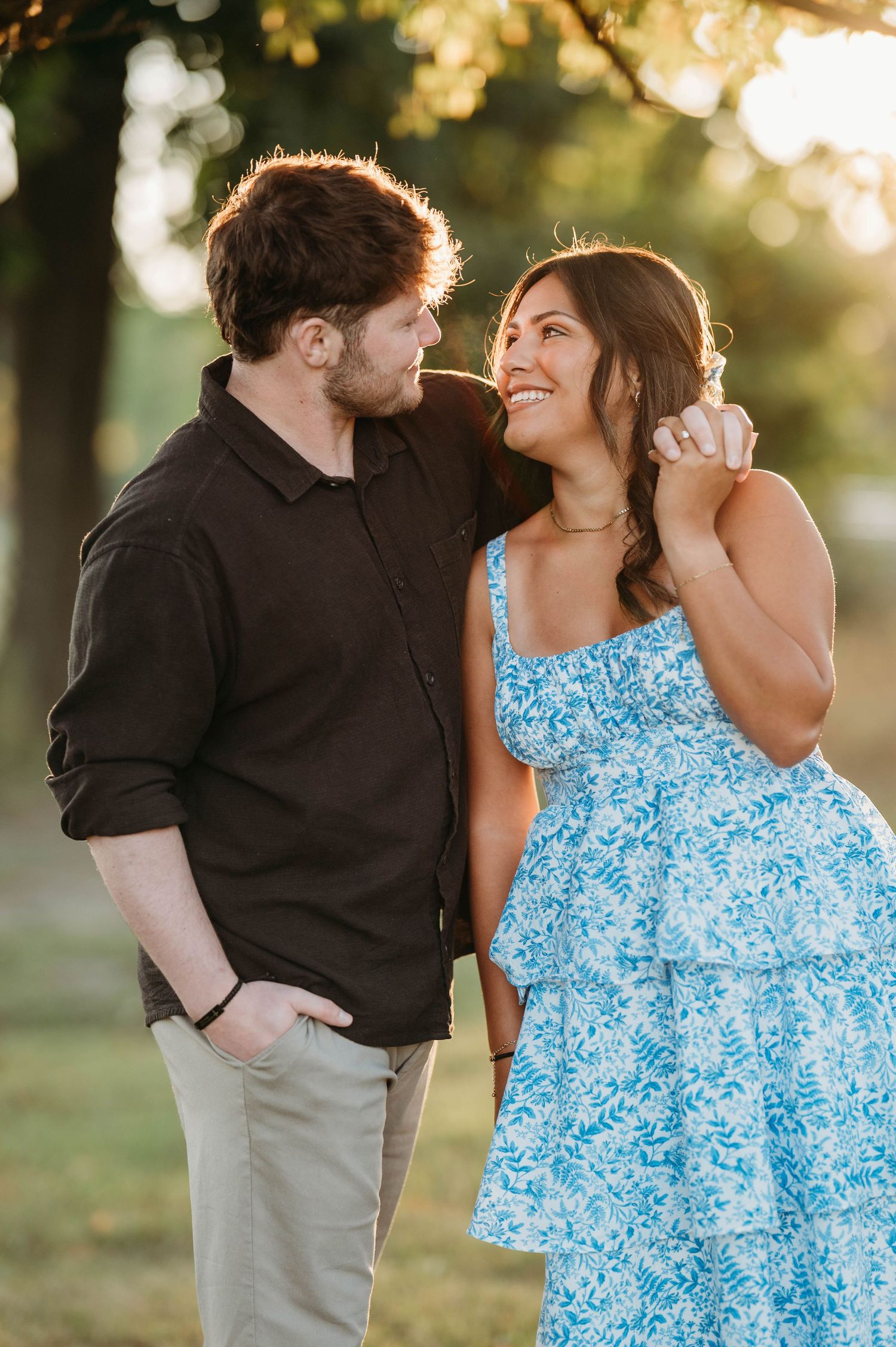 Intimate couple embracing in a park setting during golden hour, with woman in blue patterned sundress.