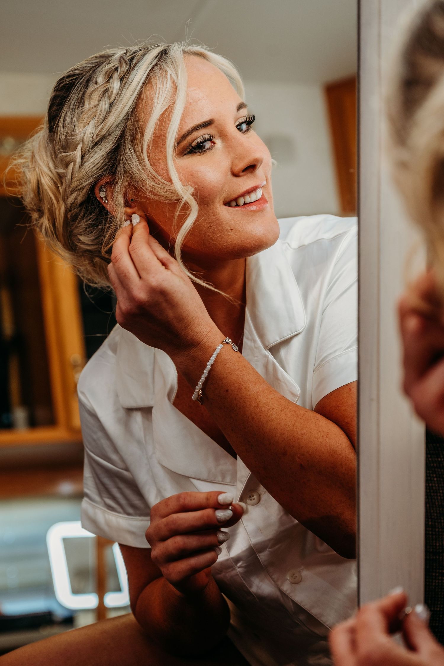Close-up of someone putting on jewelry while wearing a white top and elegant updo hairstyle.