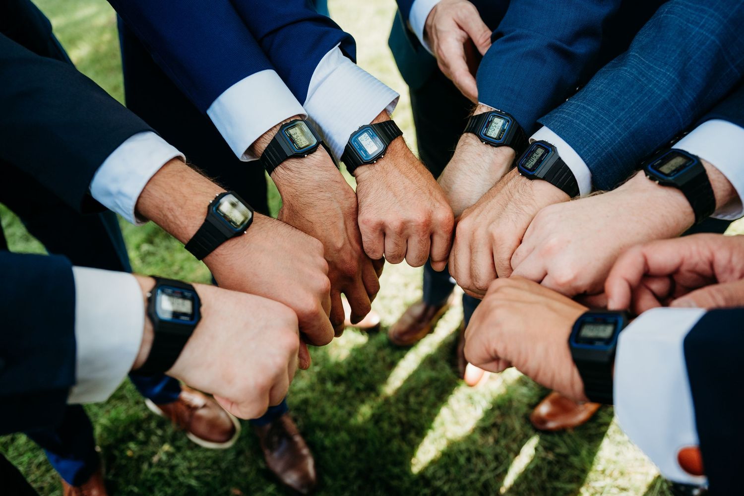 A group of hands stacked together in a circle showing unity and teamwork on a grassy background.