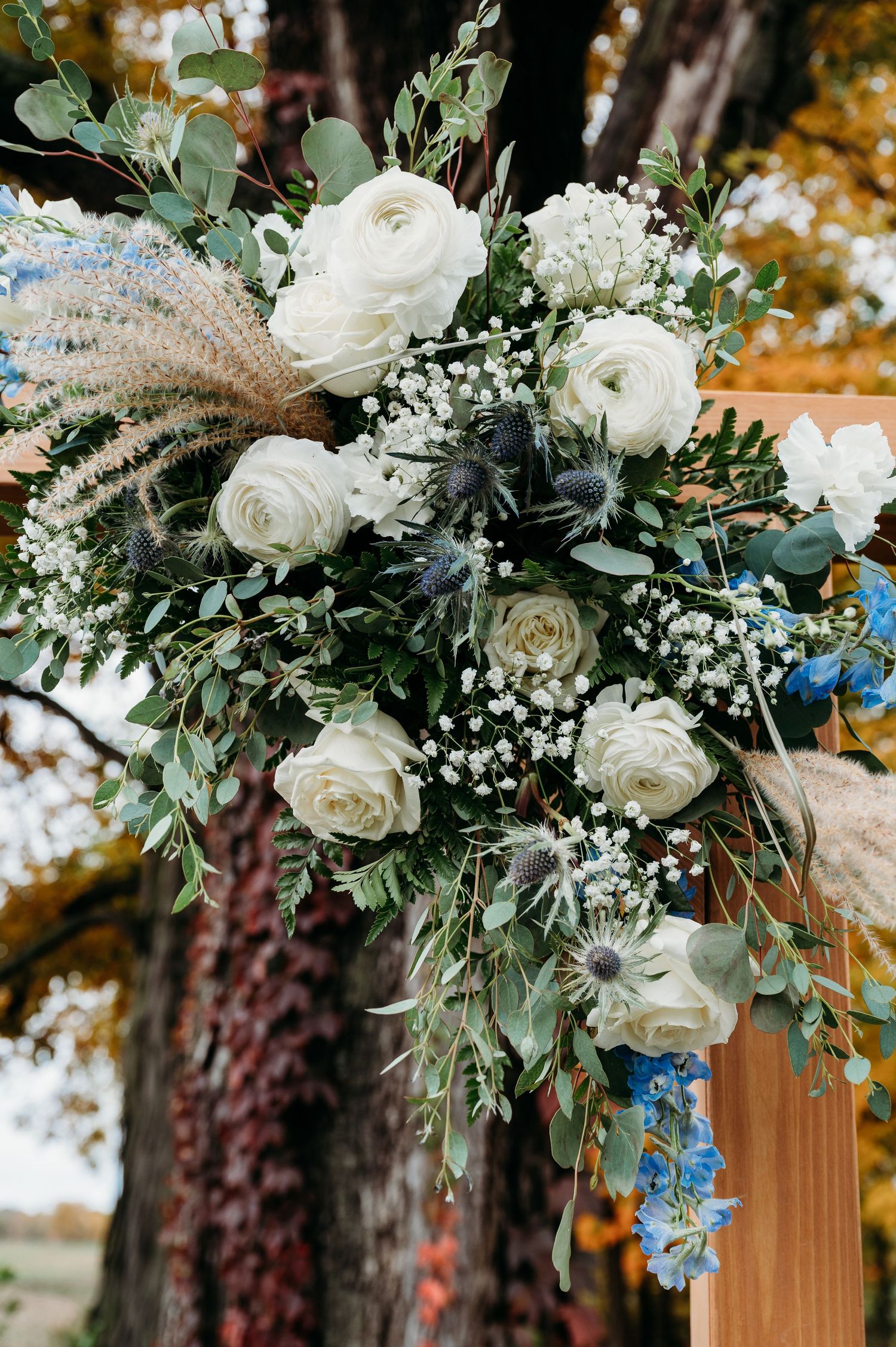Elegant white rose and baby's breath wedding bouquet with eucalyptus greenery against an autumn backdrop.