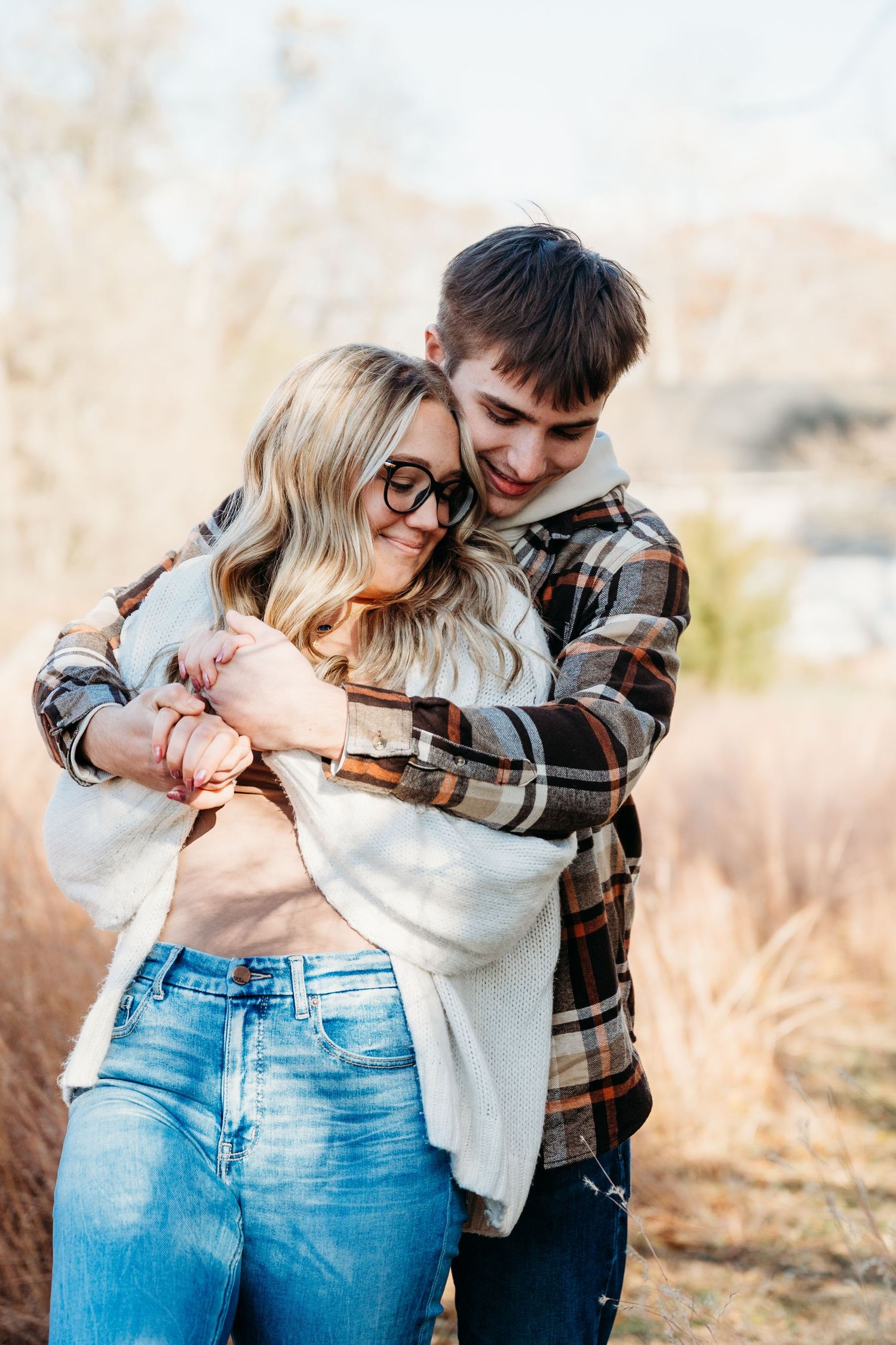 Romantic couple embraces and laughs together in casual outfits during outdoor autumn photoshoot.