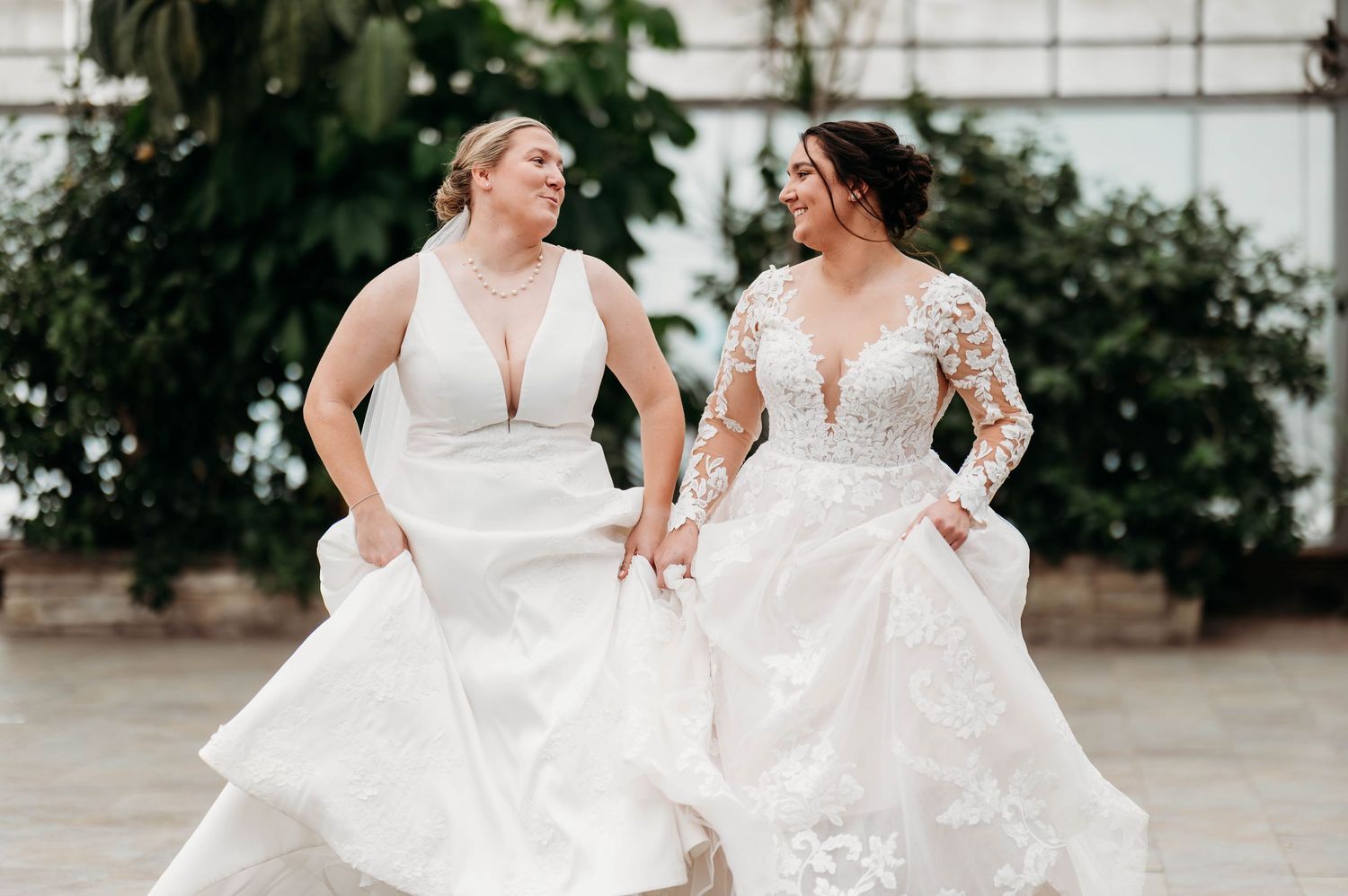 Two brides in white wedding dresses twirling and dancing together in a joyful moment.
