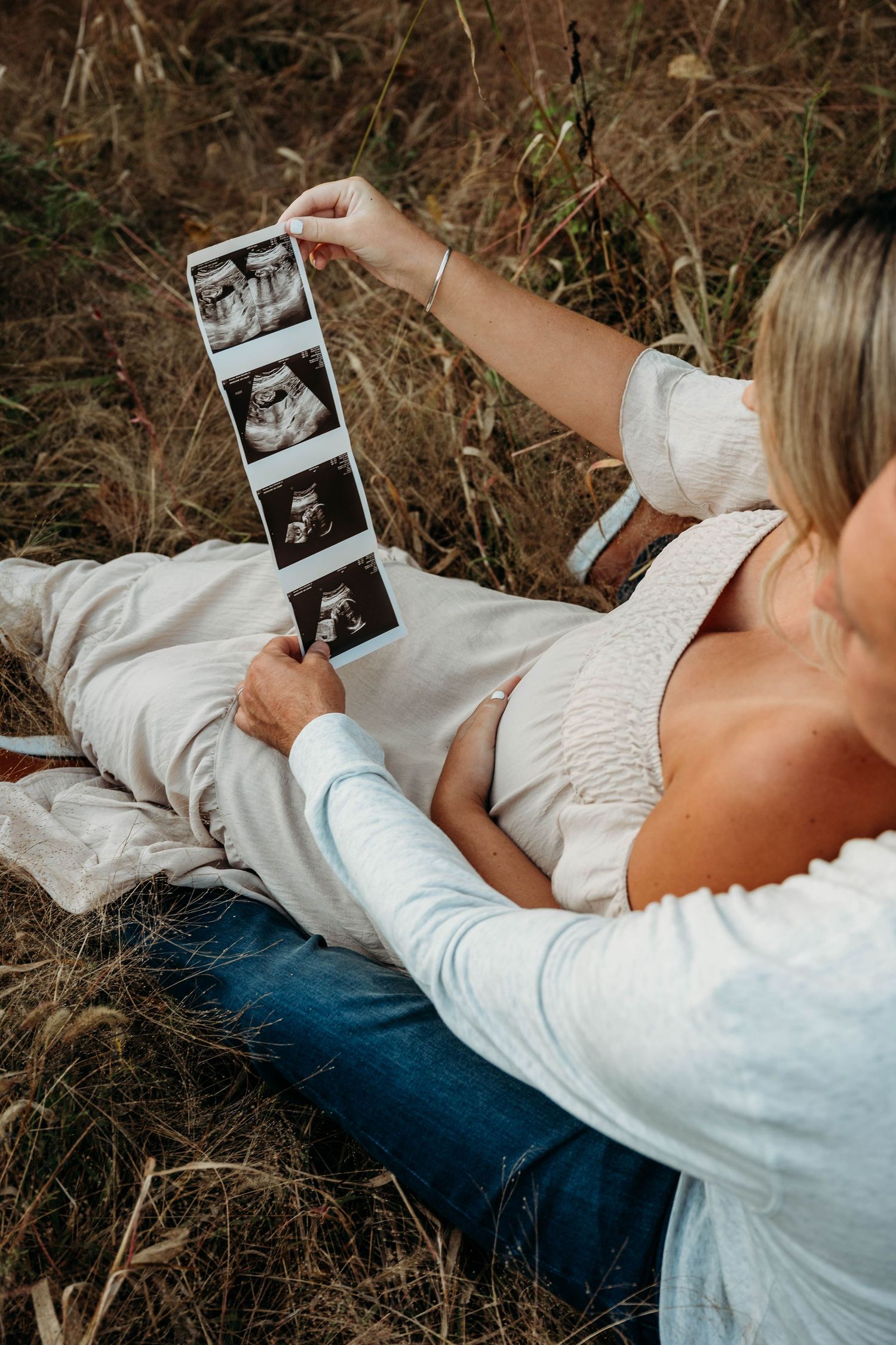 Couple lying in grass looking at ultrasound photos in a series of intimate pregnancy announcement moments.