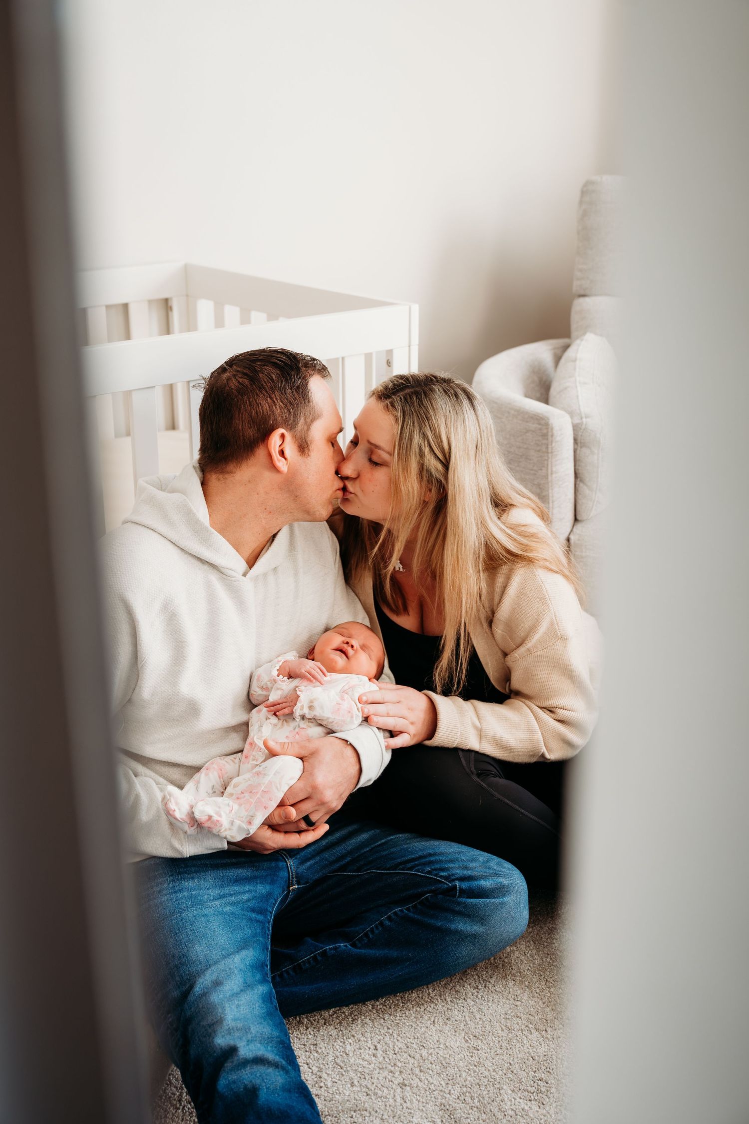Parents share tender moments with their newborn baby while sitting together on a carpeted floor.